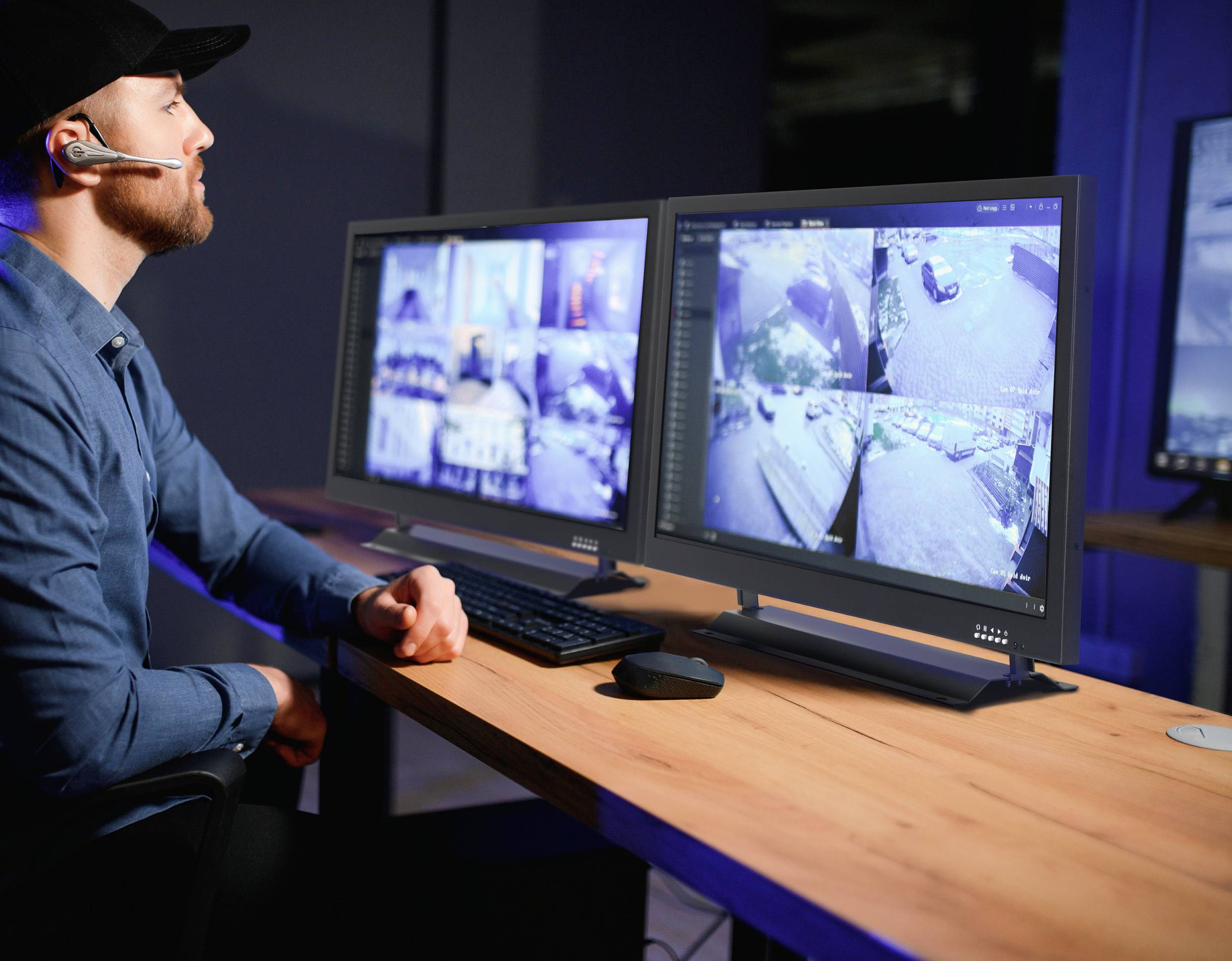 Eine Person mit einem Headset überwacht mehrere Sicherheitsaufnahmen auf zwei Computerbildschirmen in einer Kontrollraumumgebung.