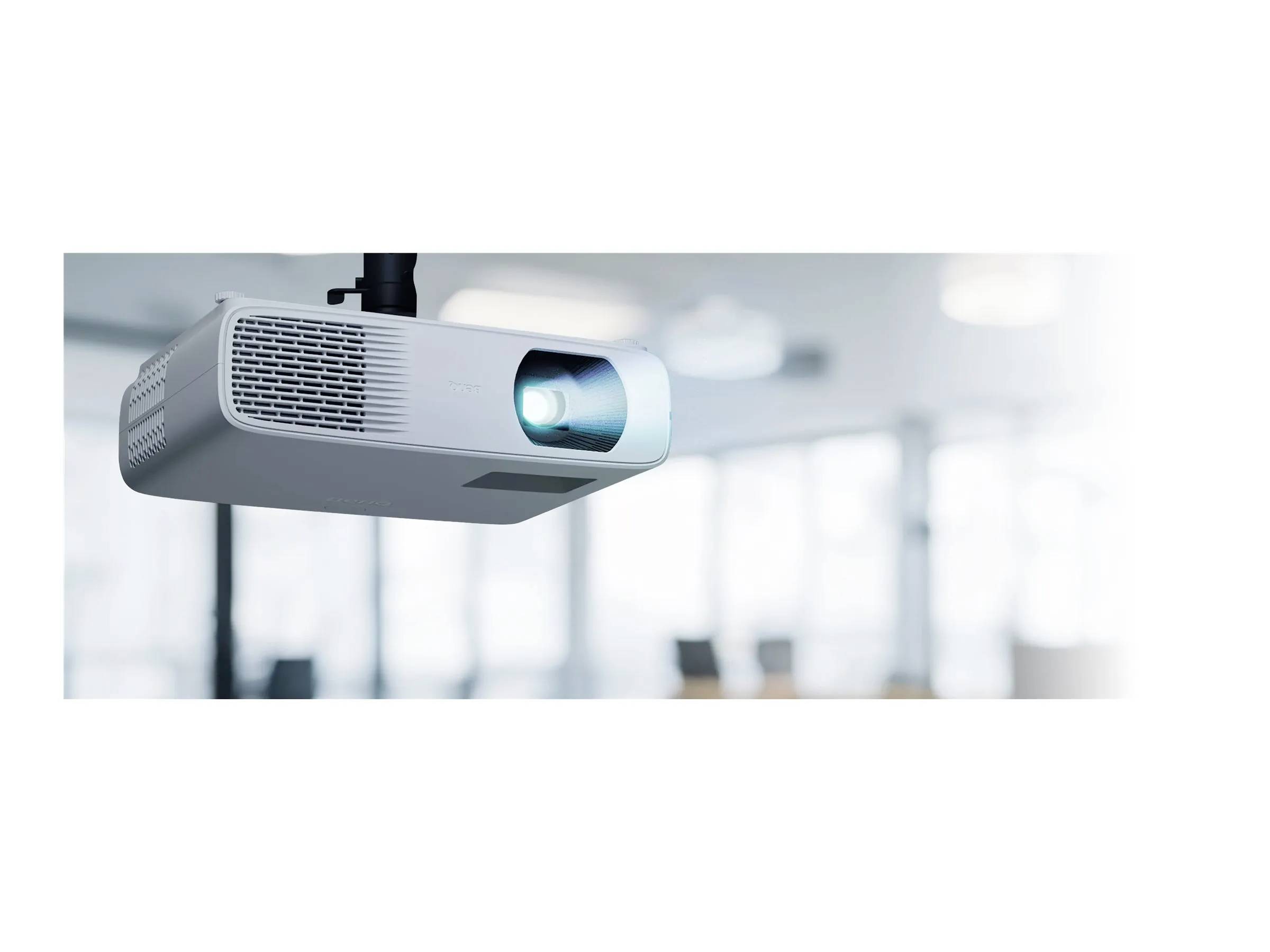 Ein an der Decke montierter Projektor ist aktiv und projiziert blaues Licht in einer hellen Büroumgebung mit unscharfen Hintergrundelementen.