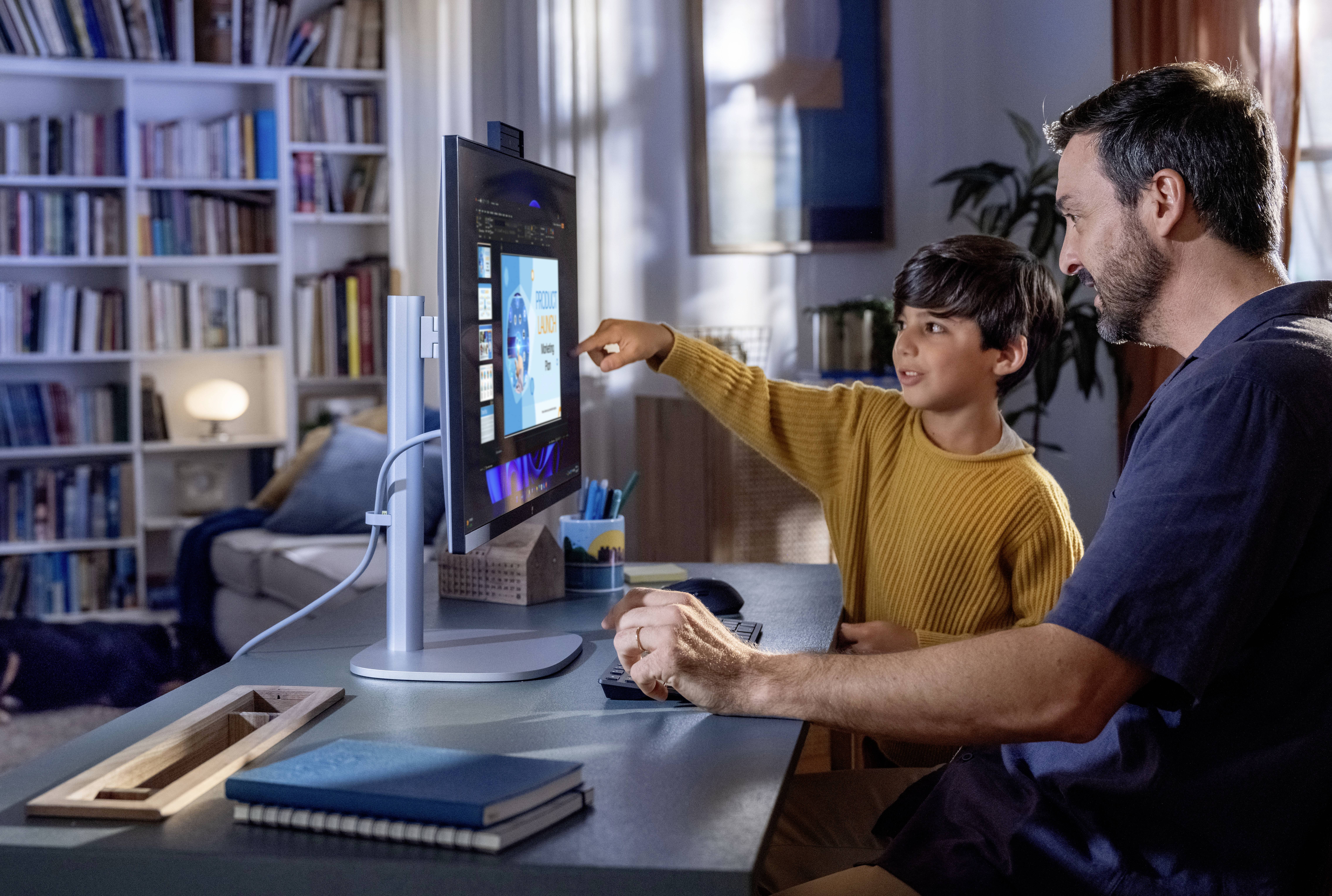 Ein Mann und ein Junge schauen gemeinsam in einem gemütlichen, mit Büchern gefüllten Raum auf einen Computerbildschirm und konzentrieren sich auf eine Bildungspräsentation.