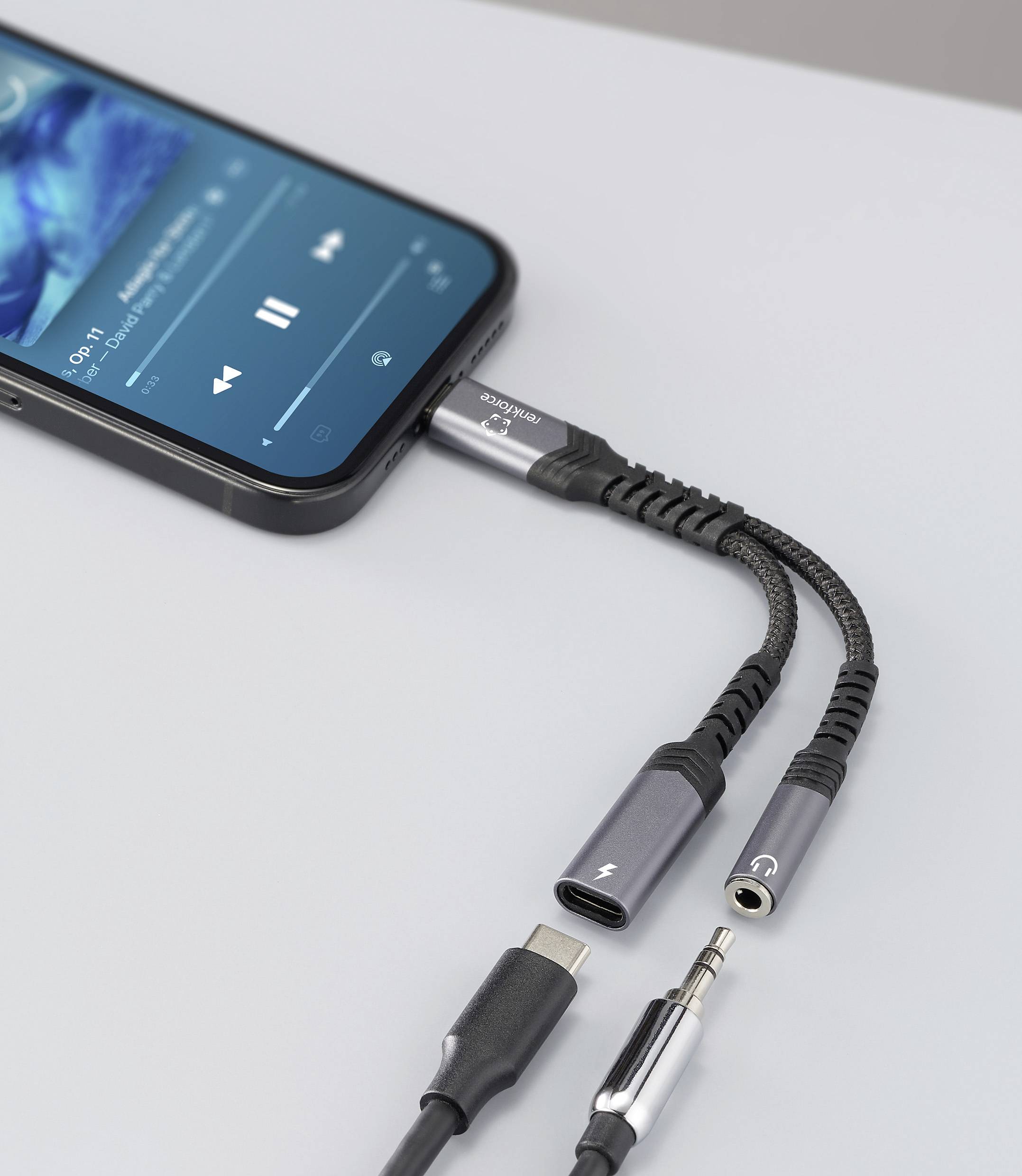 Ein Smartphone, das Musik abspielt, ist über einen Dual-Adapter mit USB-C und 3,5-mm-Klinke auf einem Tisch angeschlossen.