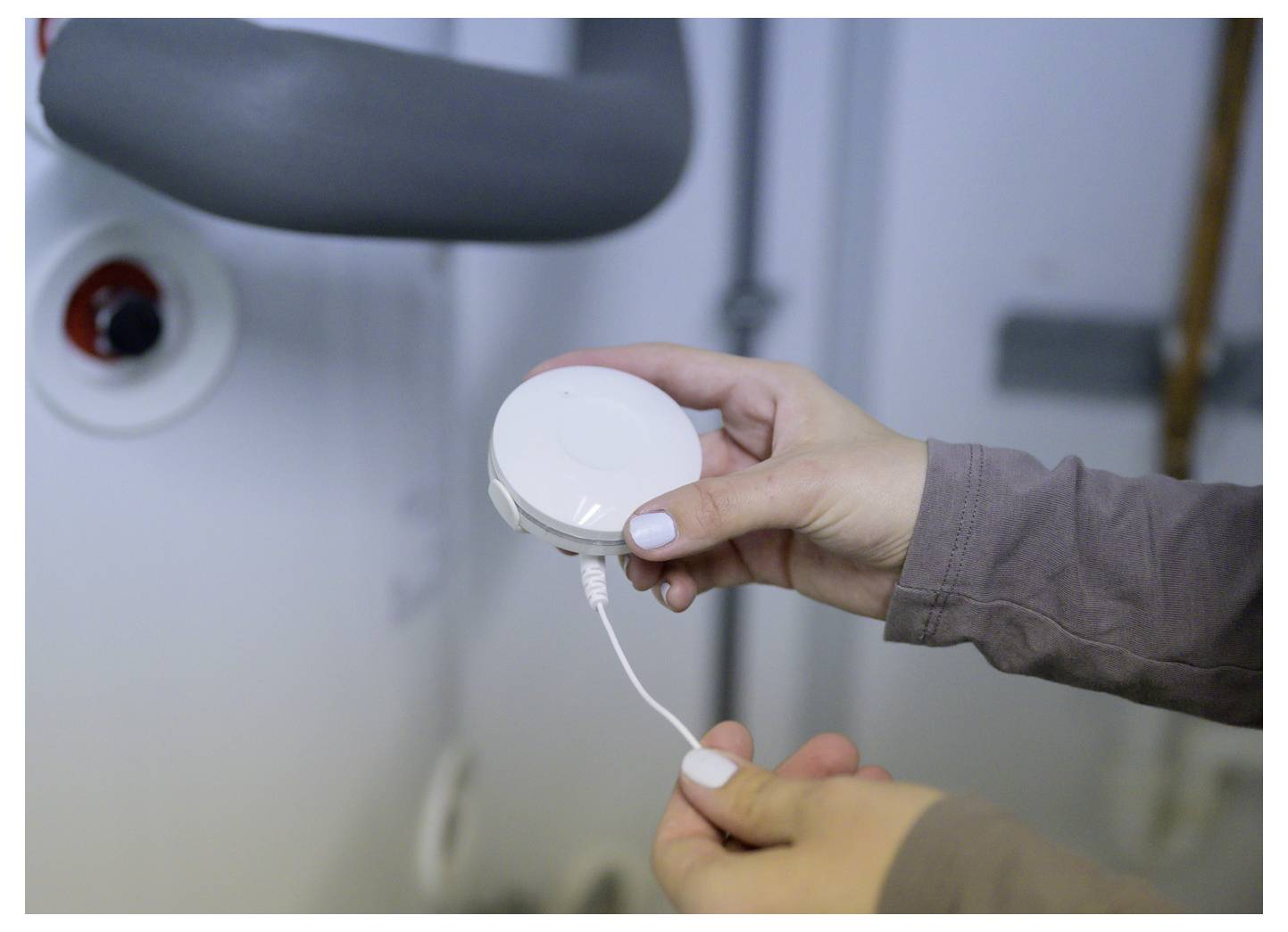 Hände, die ein weißes Ladekabel in ein kleines rundes Gerät neben einem Stuhl stecken, wahrscheinlich um medizinische oder persönliche Ausrüstung vorzubereiten.