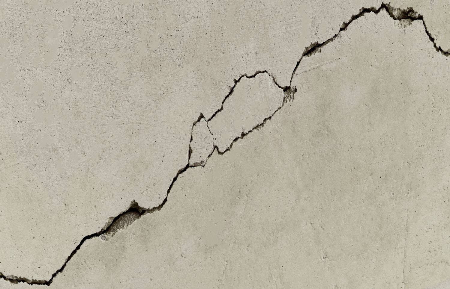 Eine beige-farbene Wand mit einem markanten Diagonal-Riss, der sich quer über sie erstreckt und auf Schäden oder strukturelle Probleme hindeutet.