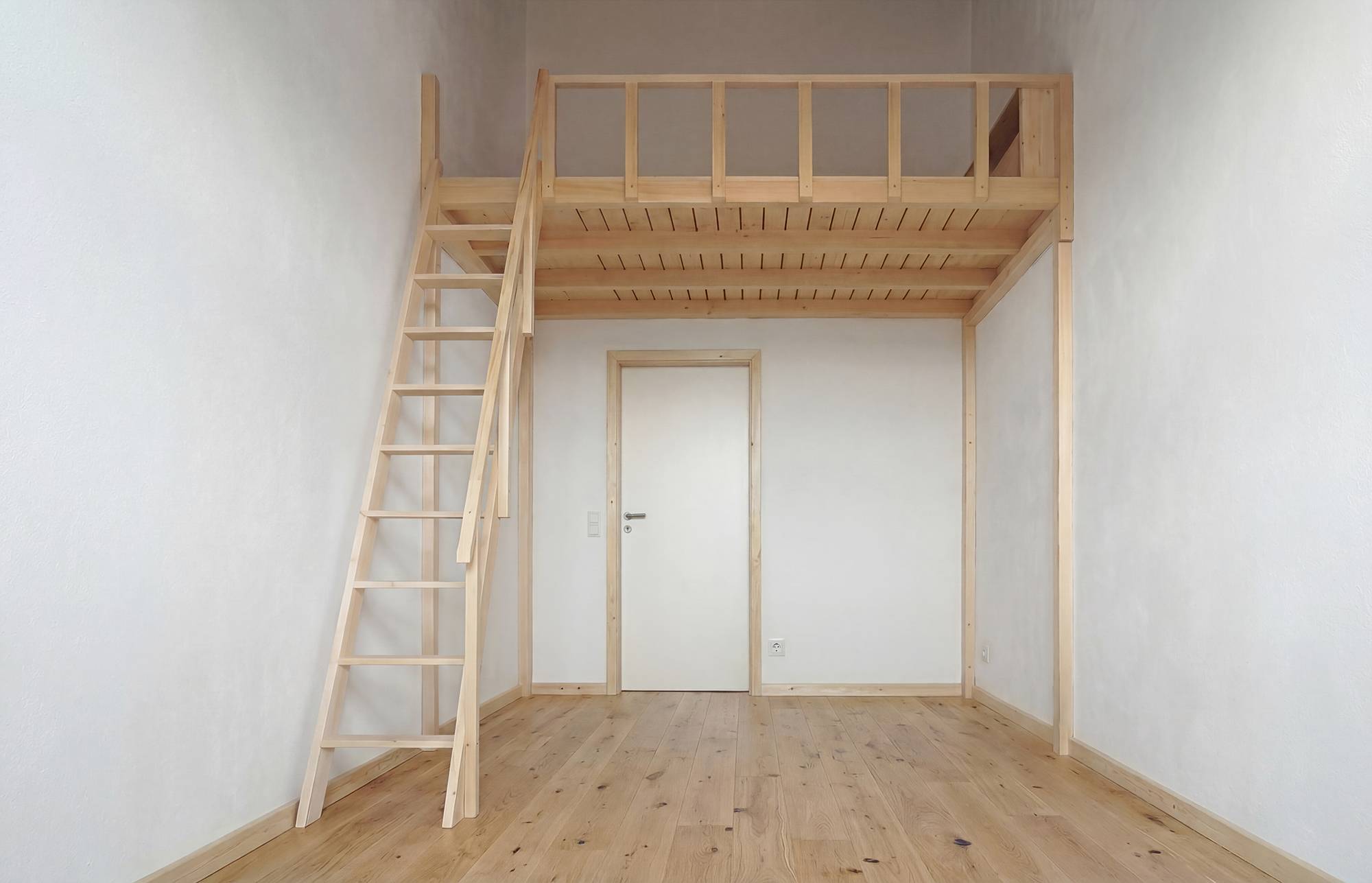 Leeres Loft-Zimmer mit hölzerner Hochbettplattform und Leiter an einer weißen Wand, sowie einer geschlossenen Tür unter dem Hochbett.