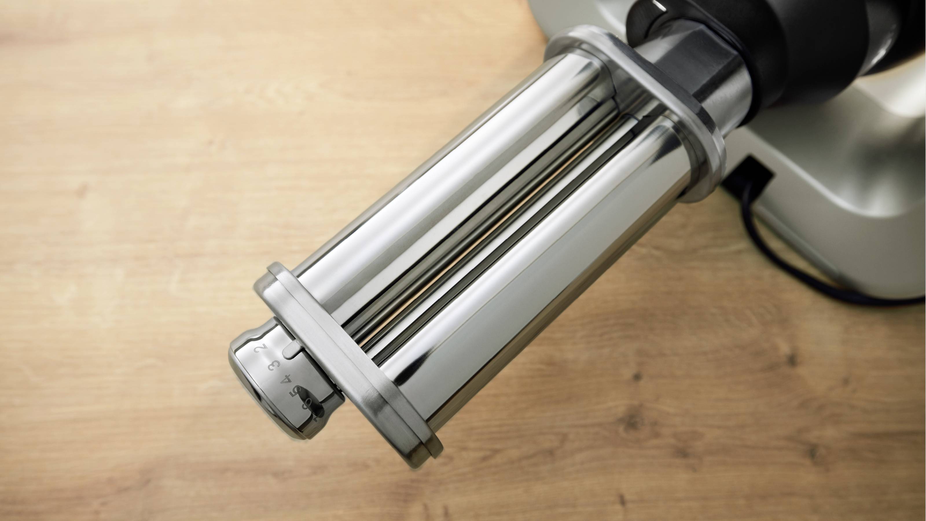 Eine Nudelmaschine mit glänzendem Metallwalzwerk steht auf einer Holzoberfläche und ist bereit, hausgemachte Nudeln herzustellen.