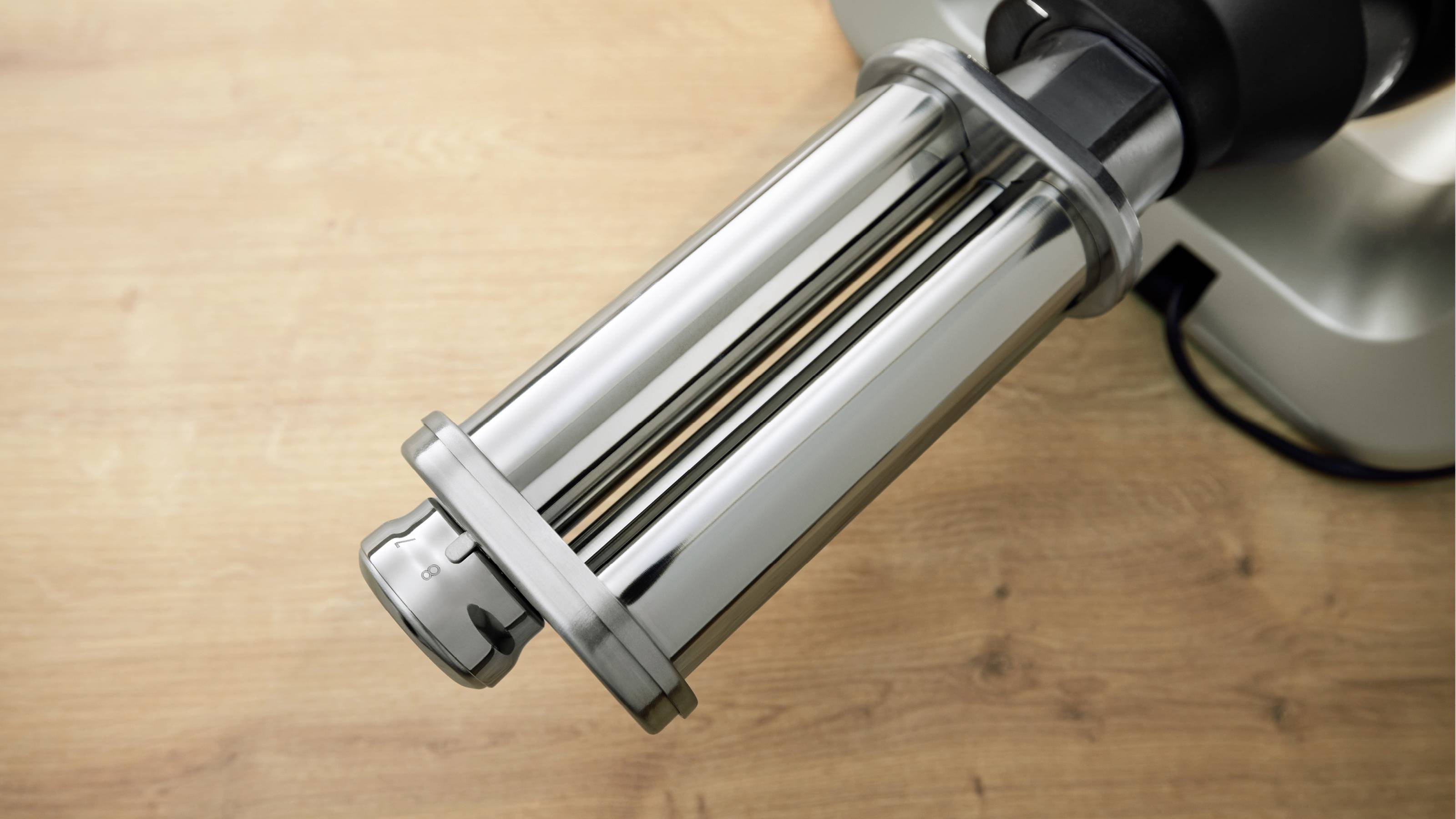 Eine Metallnudelwalze, die an einem Küchengerät befestigt ist und auf einer Holzarbeitsplatte steht, zum Ausrollen von Nudelteig.