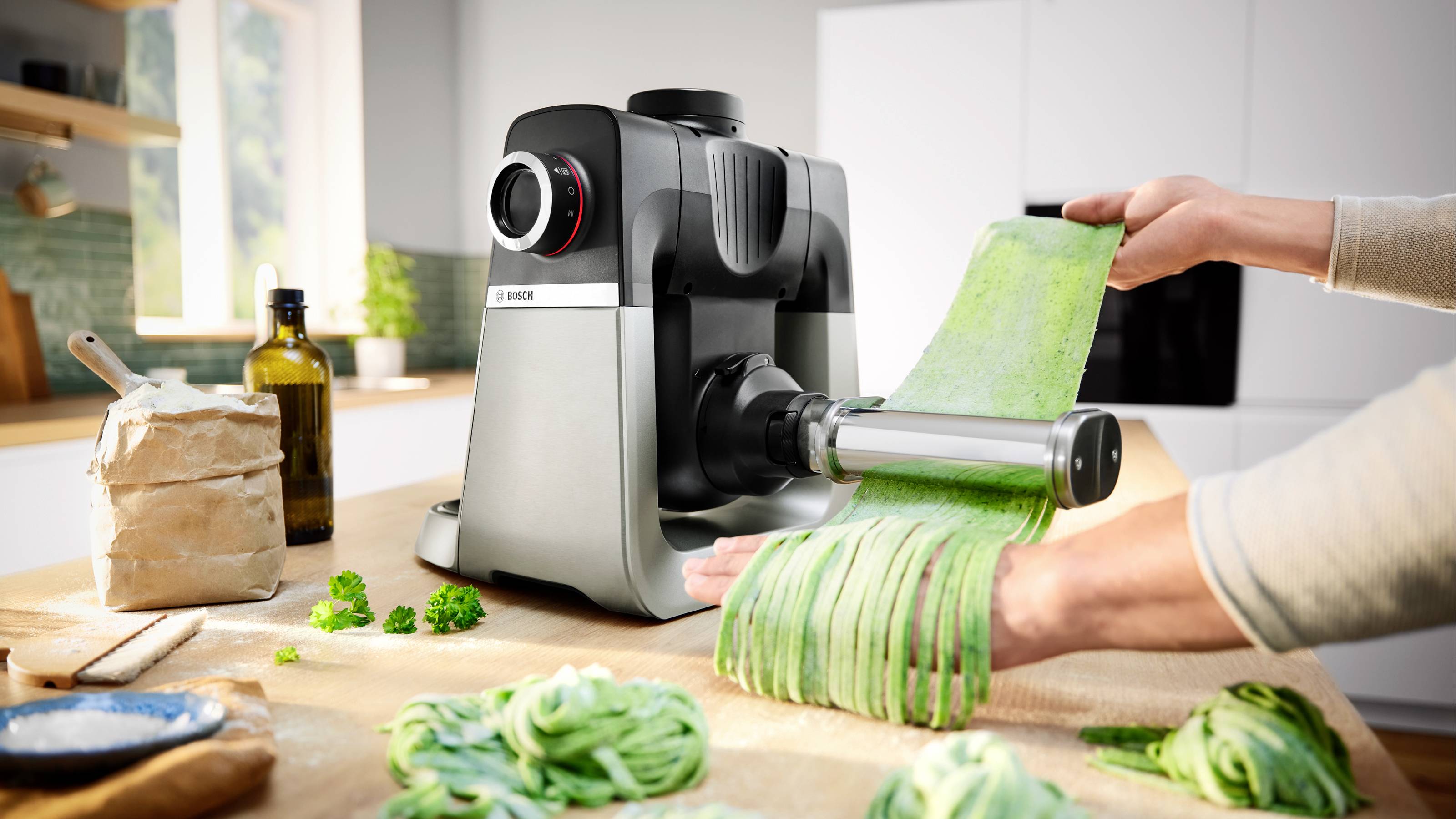 Eine Person, die frische Pasta mit einer Nudelmaschine in einer Küche herstellt, umgeben von Zutaten wie Mehl und frischen Kräutern.