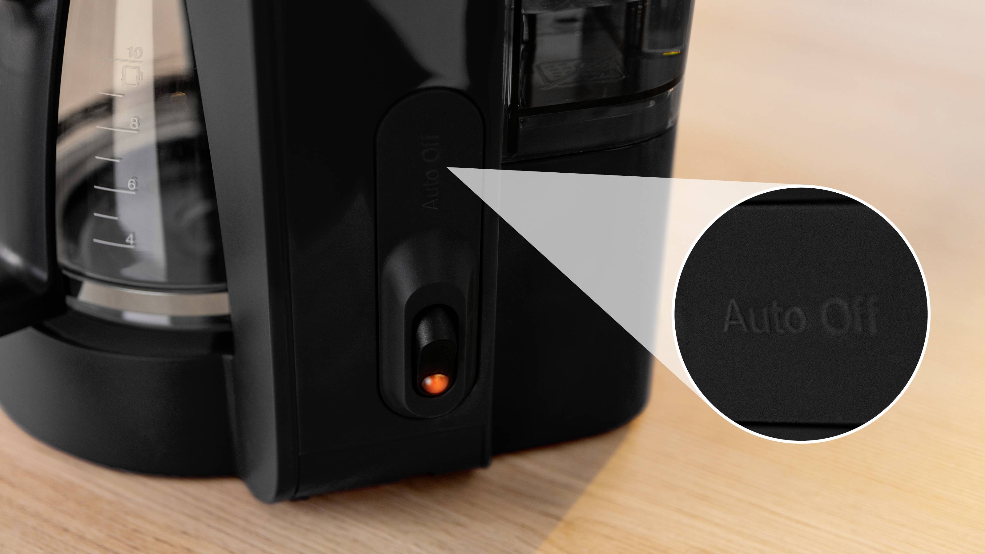 Nahaufnahme eines Kaffeemachers mit hervorgehobenem 'Auto-Aus' Knopf, der die automatische Abschaltfunktion betont, auf einer Holzoberfläche platziert.