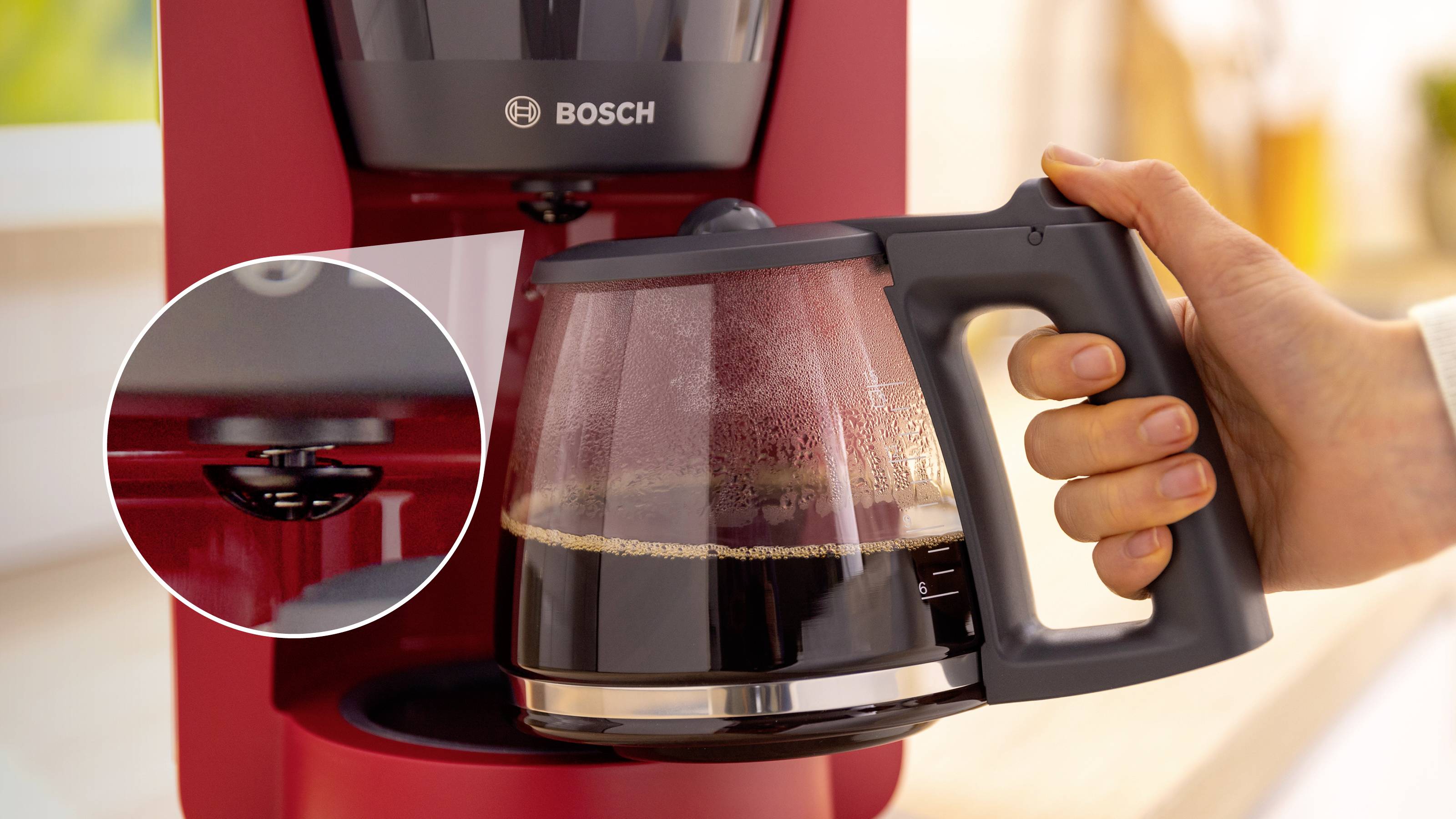 Eine Person hält eine Glaskanne mit gebrühtem Kaffee, die aus einer roten Kaffeemaschine stammt. Eine Nahaufnahme zeigt einen Auslöseknopf.