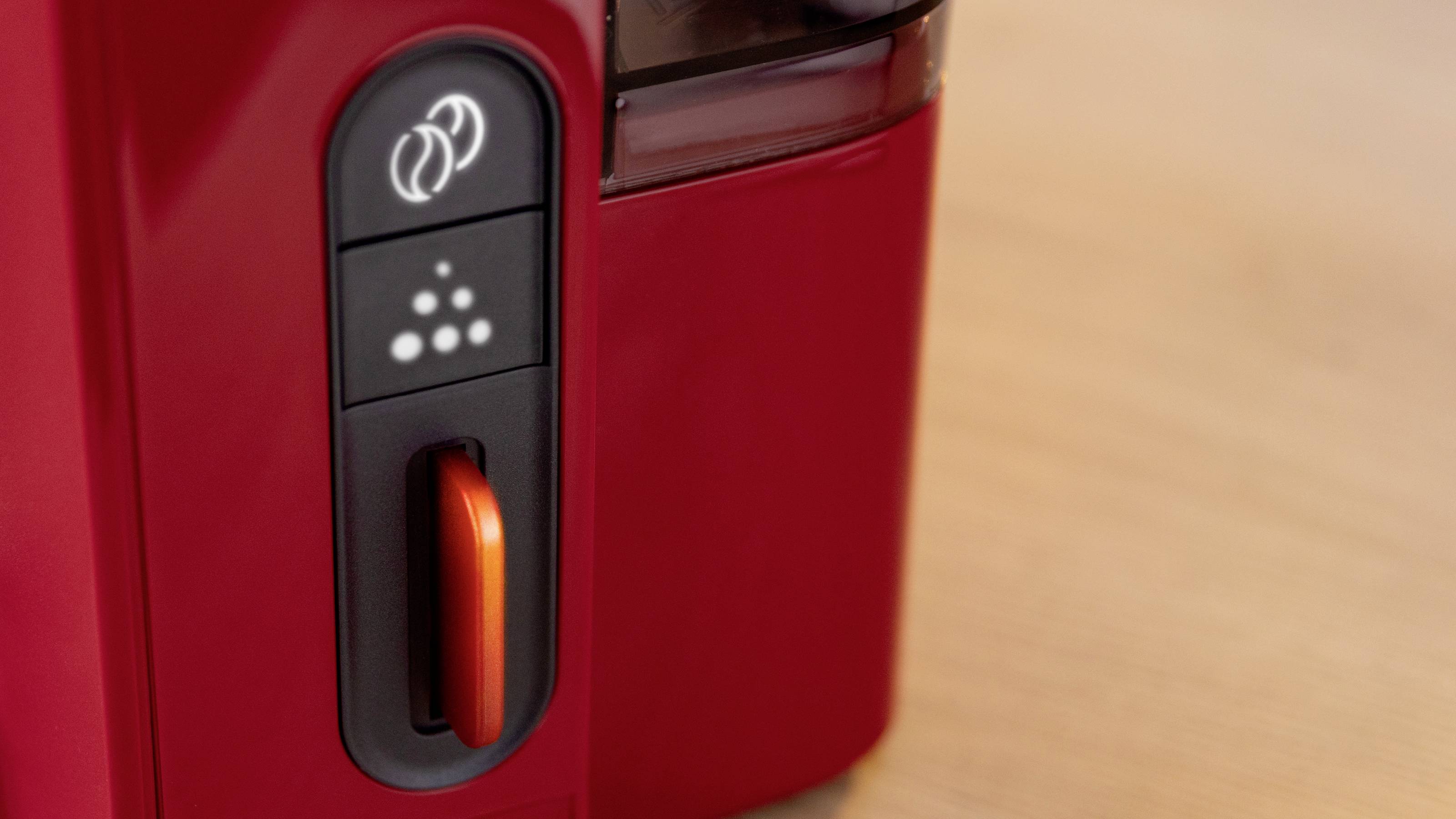 Eine Nahaufnahme des Bedienfelds einer roten Kaffeemaschine mit Tasten und einem Drehregler. Das Panel enthält Symbole für verschiedene Brühoptionen.