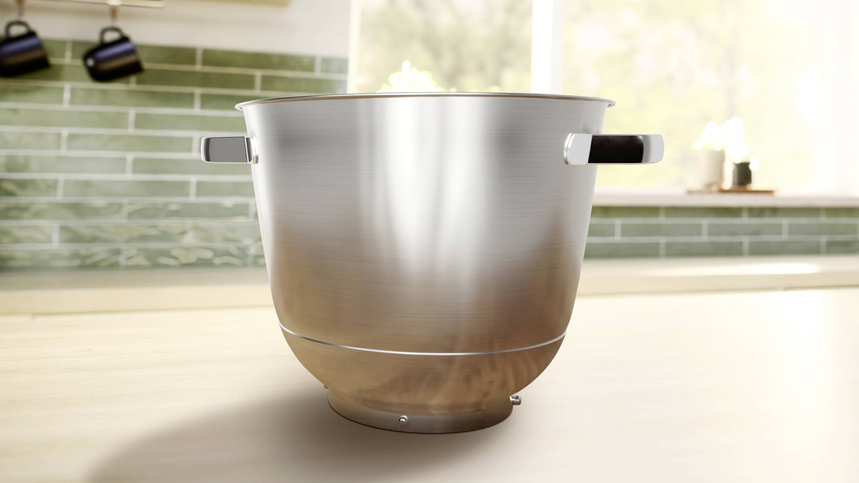 Eine große Edelstahlschüssel mit Griffen, die auf einer Küchenarbeitsplatte mit einem grünen Fliesenspiegel und einem hellen Fenster im Hintergrund steht.