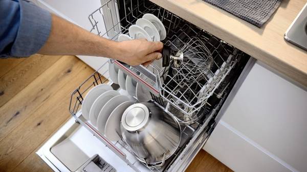 Eine Person lädt Geschirr und Kochutensilien in einen offenen Geschirrspüler in einer Küche und demonstriert eine effiziente Anordnung für eine optimale Reinigung.