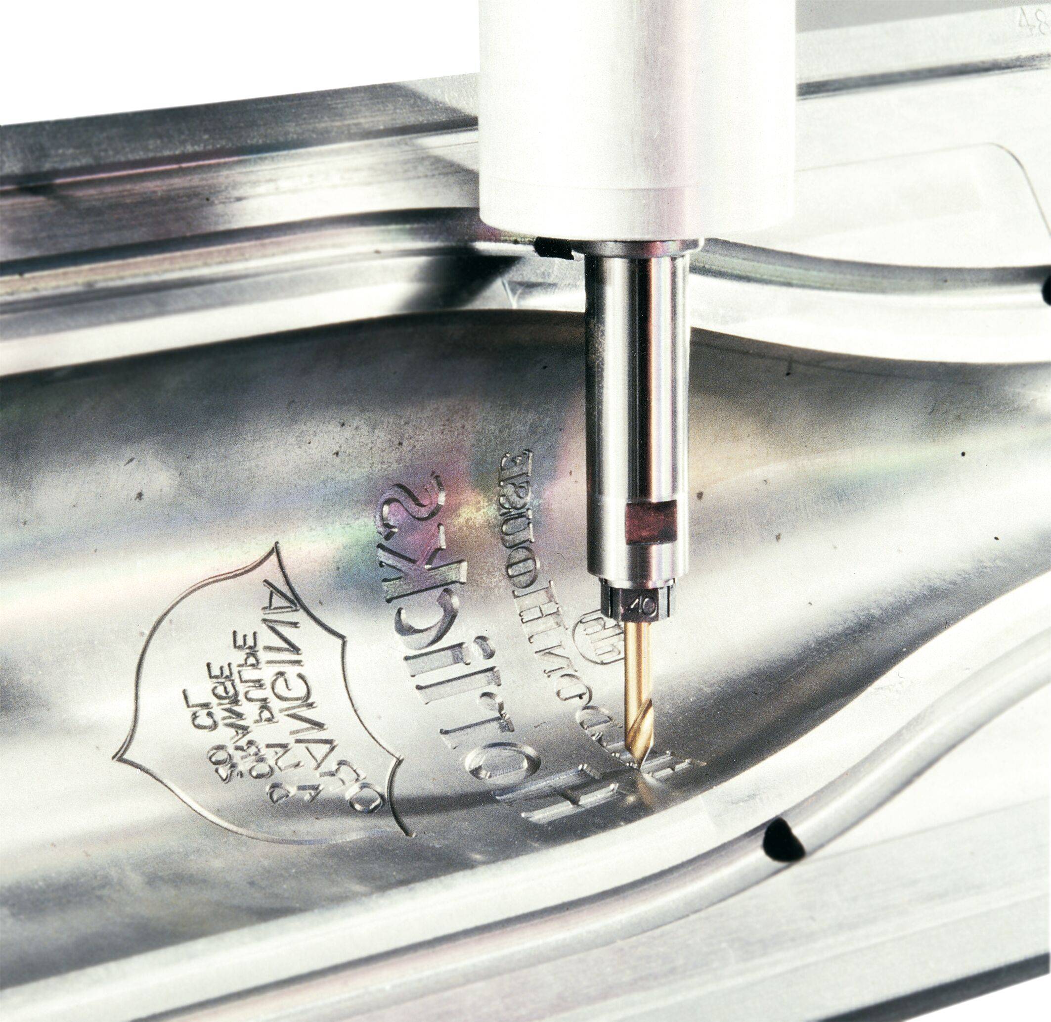 Eine CNC-Maschine graviert Text auf einer Metalloberfläche und demonstriert präzise Fertigungstechniken in industriellen Umgebungen.