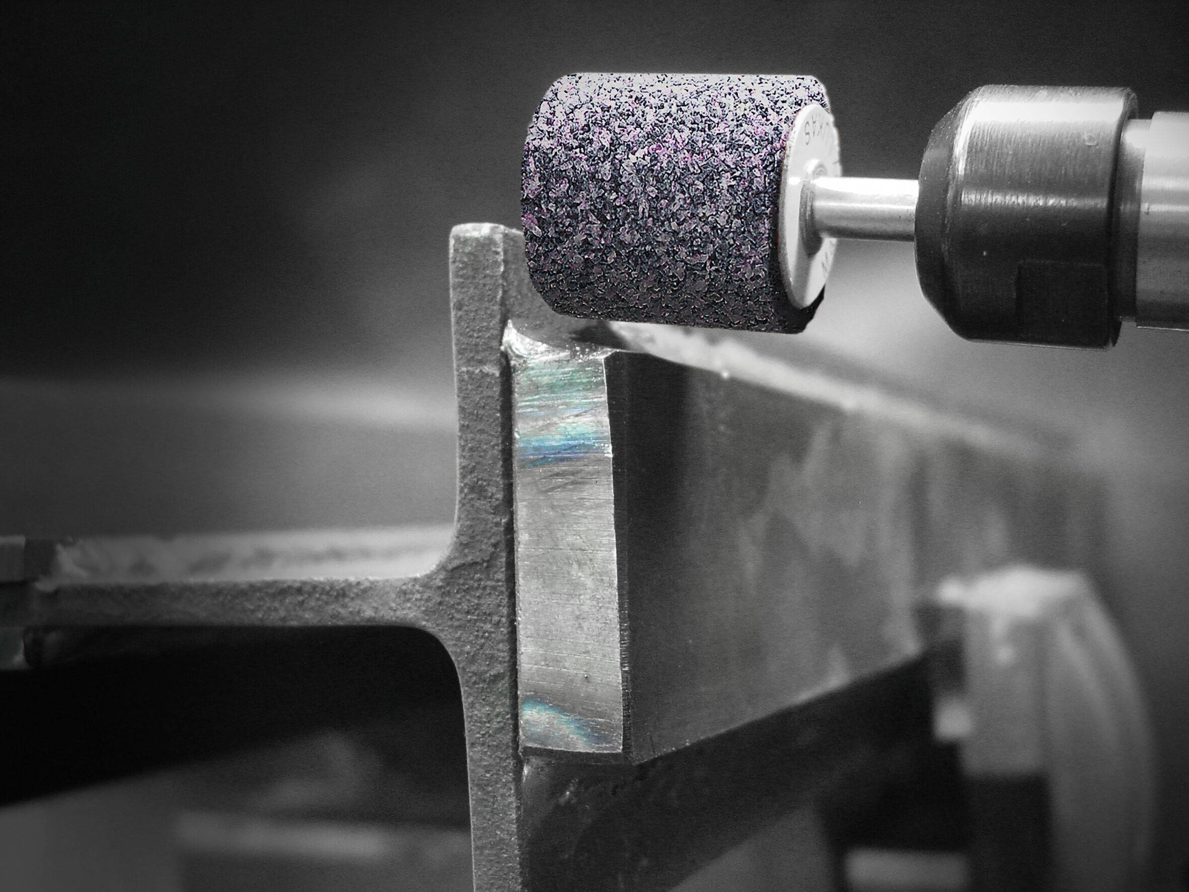 Eine Nahaufnahme einer Schleifmaschine, die die Kante eines Metallstücks glättet, wobei Funken auf aktive Arbeit hinweisen.