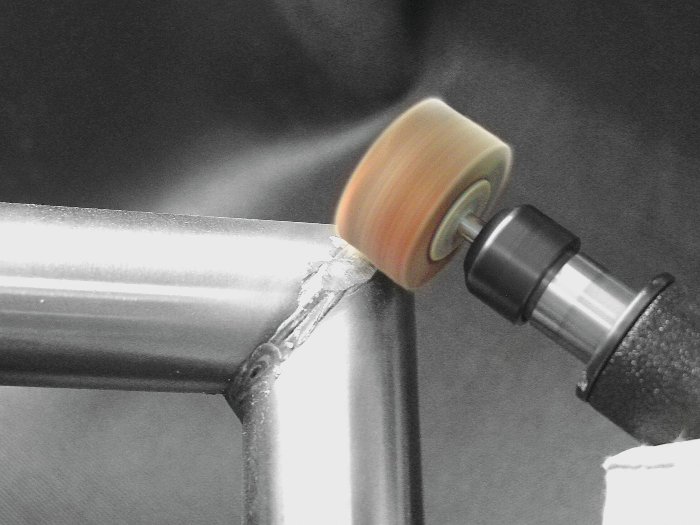 Eine Elektrowerkzeug glättet die raue Kante einer geschweißten Metallverbindung und erzeugt eine polierte Oberfläche an einem Metallrahmen vor einem dunklen Hintergrund.