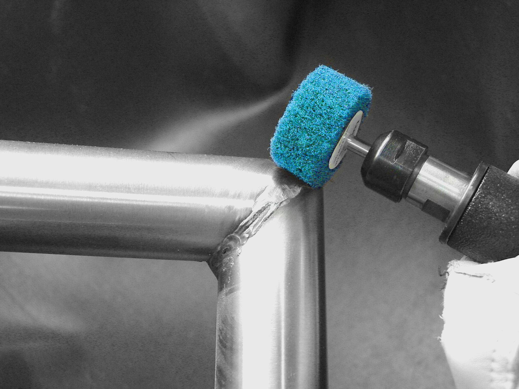 Ein blauer Schleifstein poliert die Schweißnaht zweier Stahlrohre und glättet die Oberfläche vor einem dunklen Hintergrund.