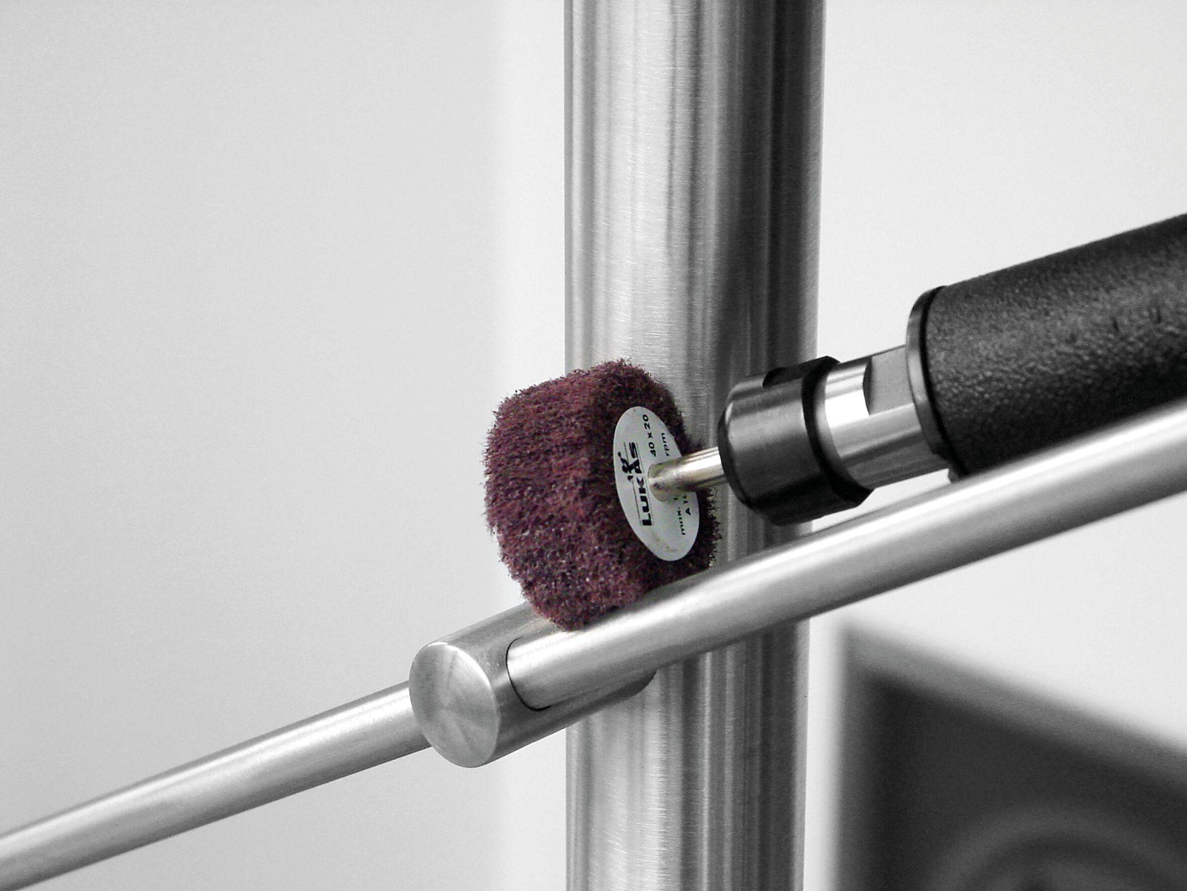 Ein Metallpolierwerkzeug wird bei der Arbeit gezeigt, während es eine Edelstahloberfläche glättet. Der zylindrische Polisher ist an einem tragbaren Rotationsgerät befestigt.