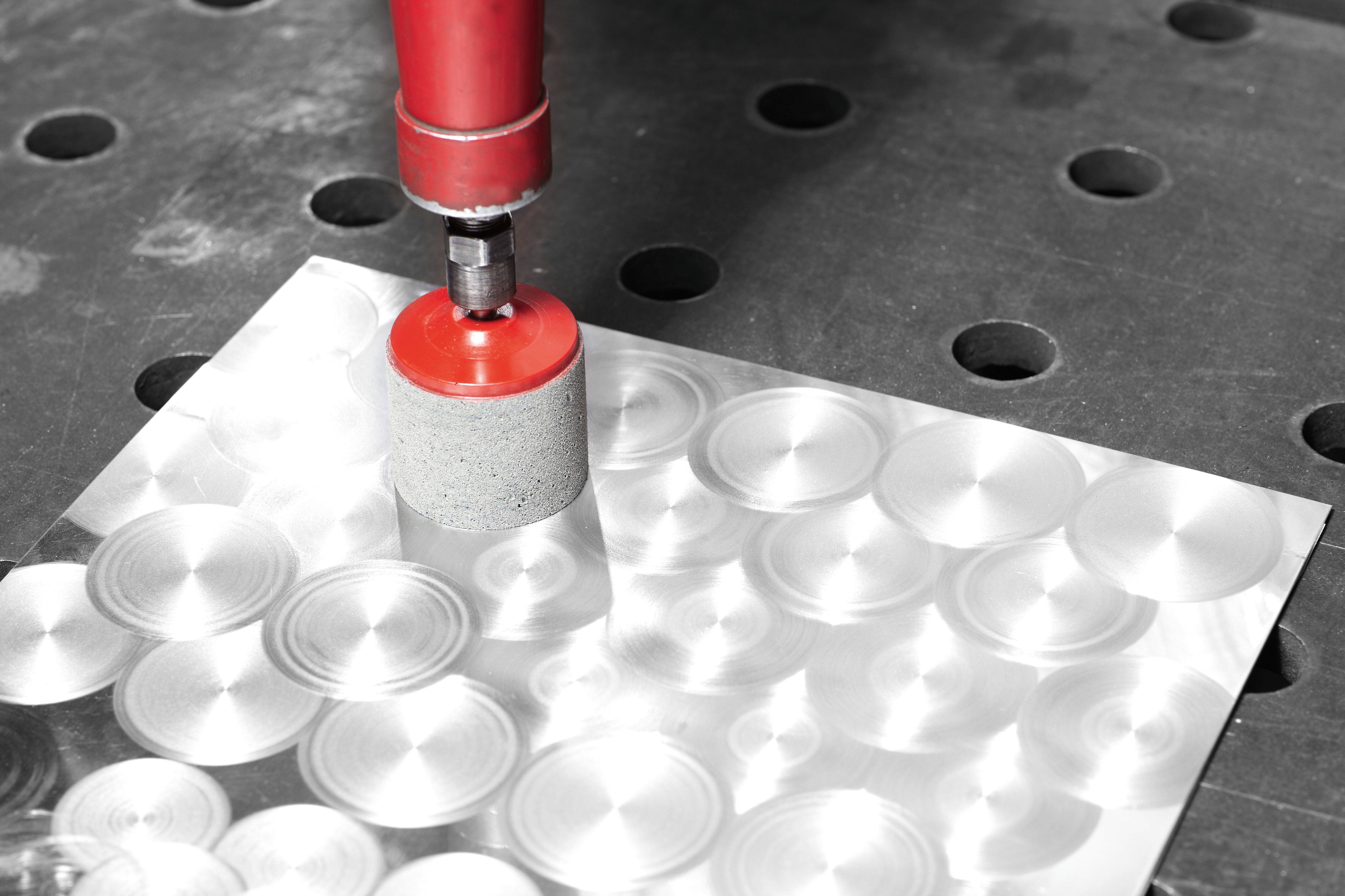 Eine rote hydraulische Presse, die kreisförmige Muster auf einem Metallblech prägt, das auf einem gelochten Metalltisch platziert ist, demonstriert die Metallbearbeitung.