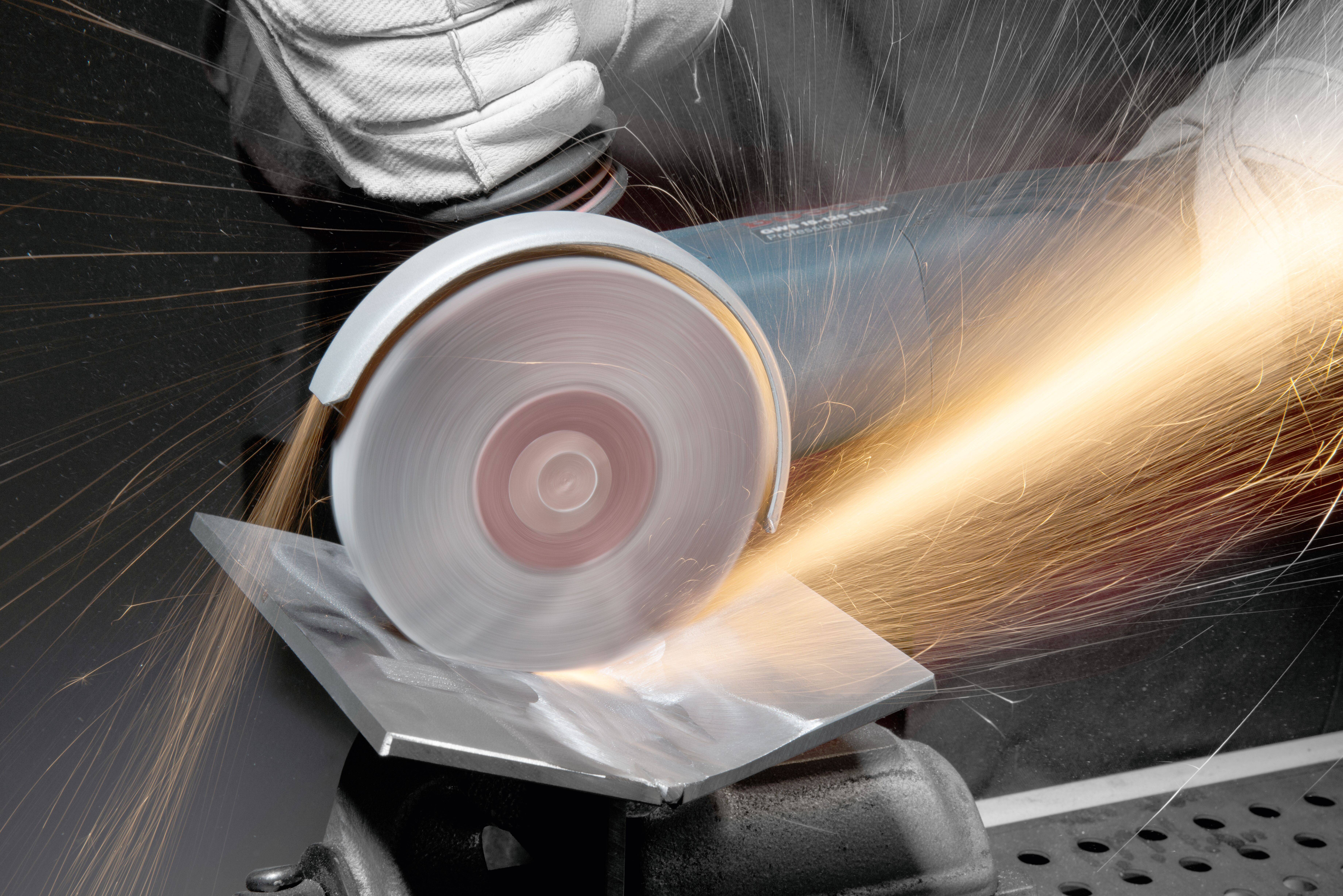 Eine Person mit Schutzhandschuhen verwendet eine Winkelschleifmaschine, um ein Metallblech zu schneiden, wobei Funken aufsprühen.