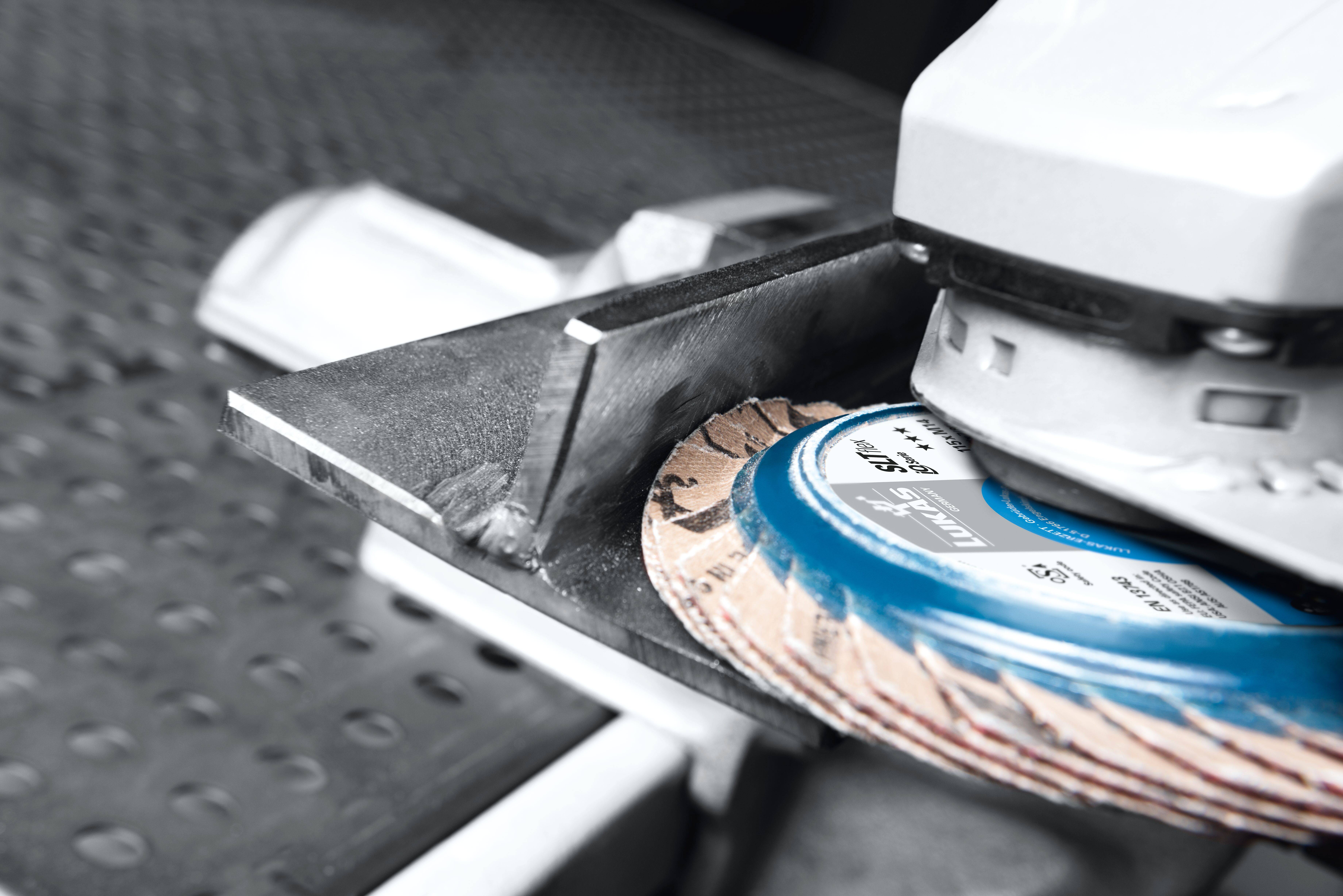 Ein metallischer Winkel, der mit einem blauen Schleifrad an einer Schleifmaschine in einer industriellen Umgebung poliert wird.