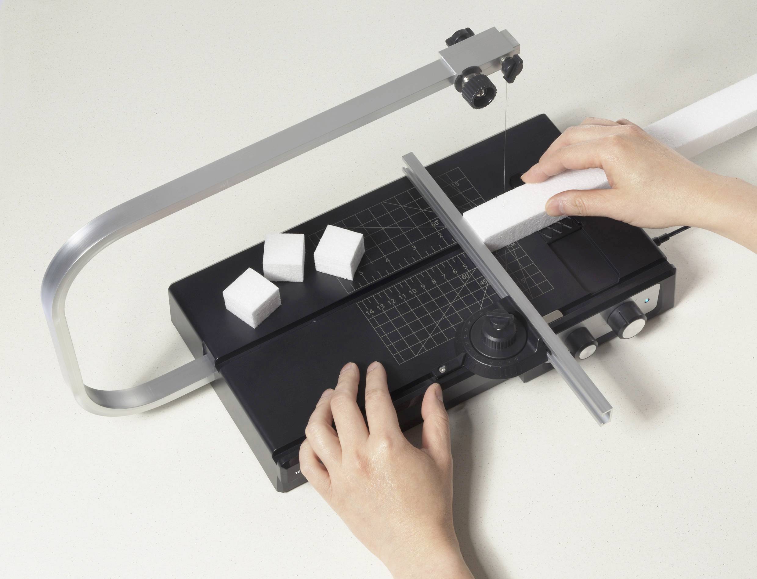 Eine Person bedient eine Schaumschneidemaschine, um einen Schaumblock zu zerschneiden. Mehrere geschnittene Stücke sind auf dem Tisch sichtbar.