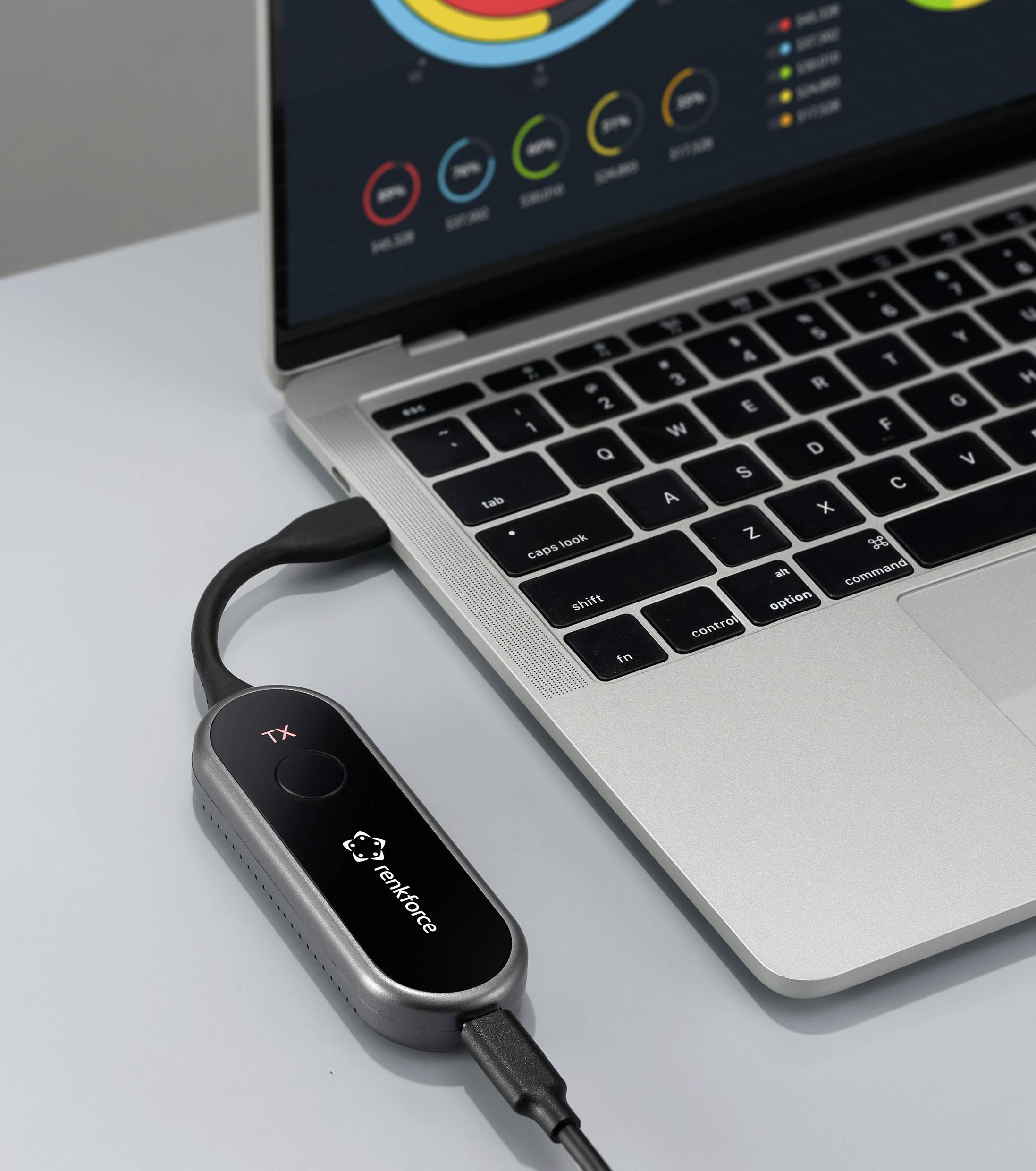 Ein Laptop auf einem Schreibtisch zeigt farbenfrohe Diagramme auf seinem Bildschirm. Ein kleines Gerät ist daneben über ein Kabel angeschlossen und zeigt ein Logo.