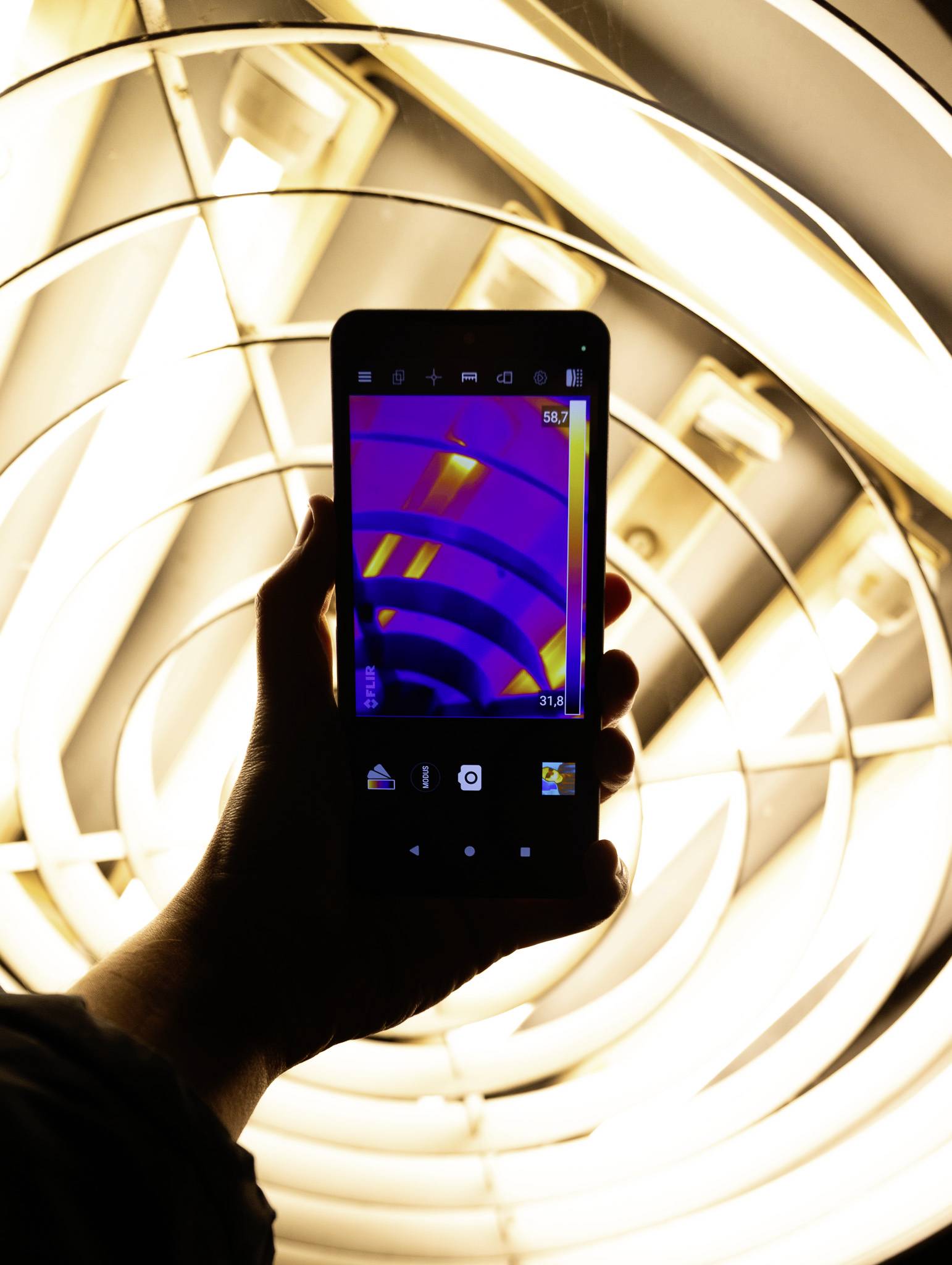 Eine Hand hält ein Smartphone, das ein lila und gelbes Wärmebild vor einem Hintergrund von hellen spiralförmigen Lichtern zeigt.