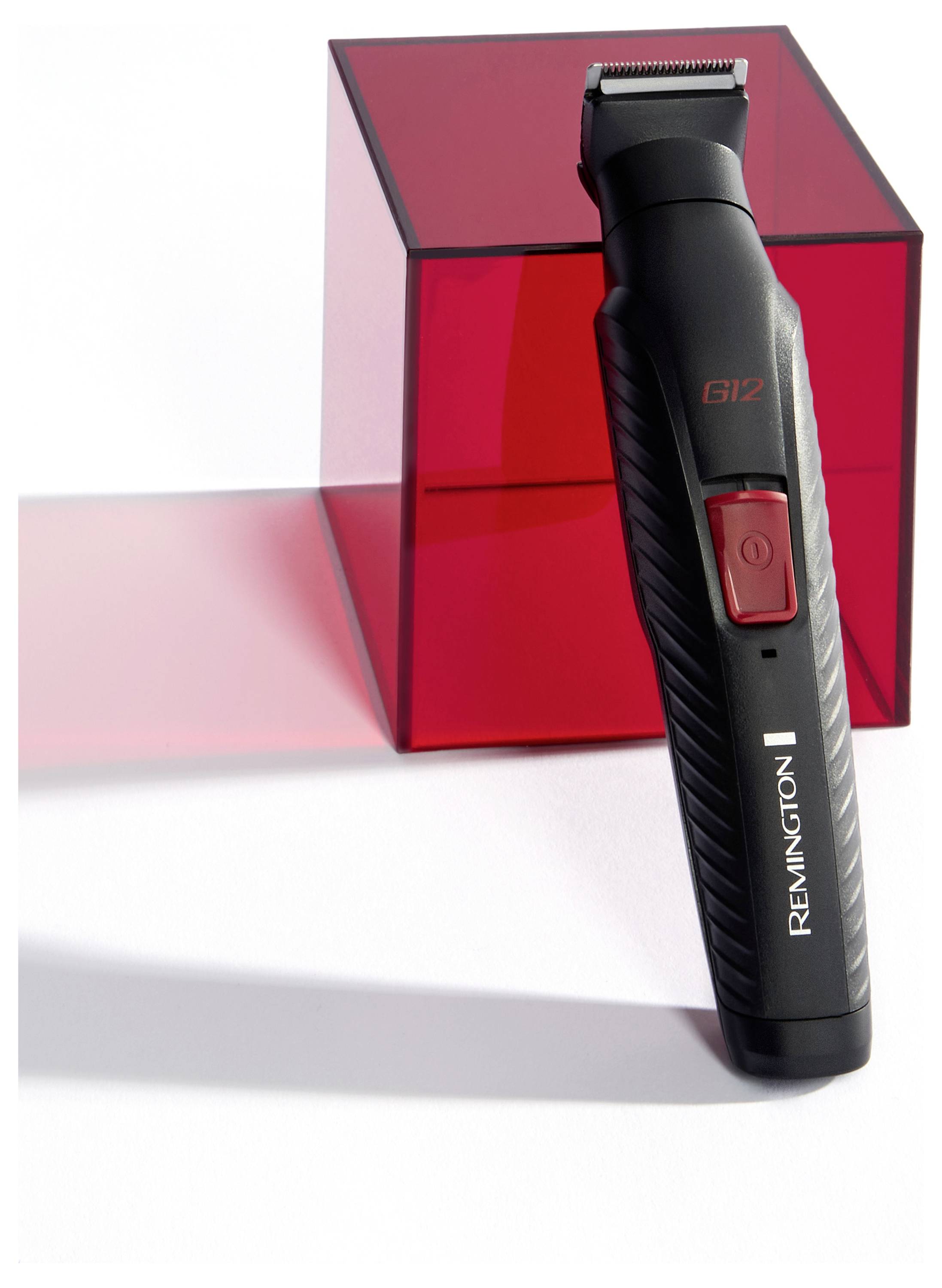 Ein schwarzer und roter elektrischer Trimmer der Marke 'Remington' steht aufrecht neben einem roten, transparenten Würfel, der Schatten auf eine weiße Oberfläche wirft.