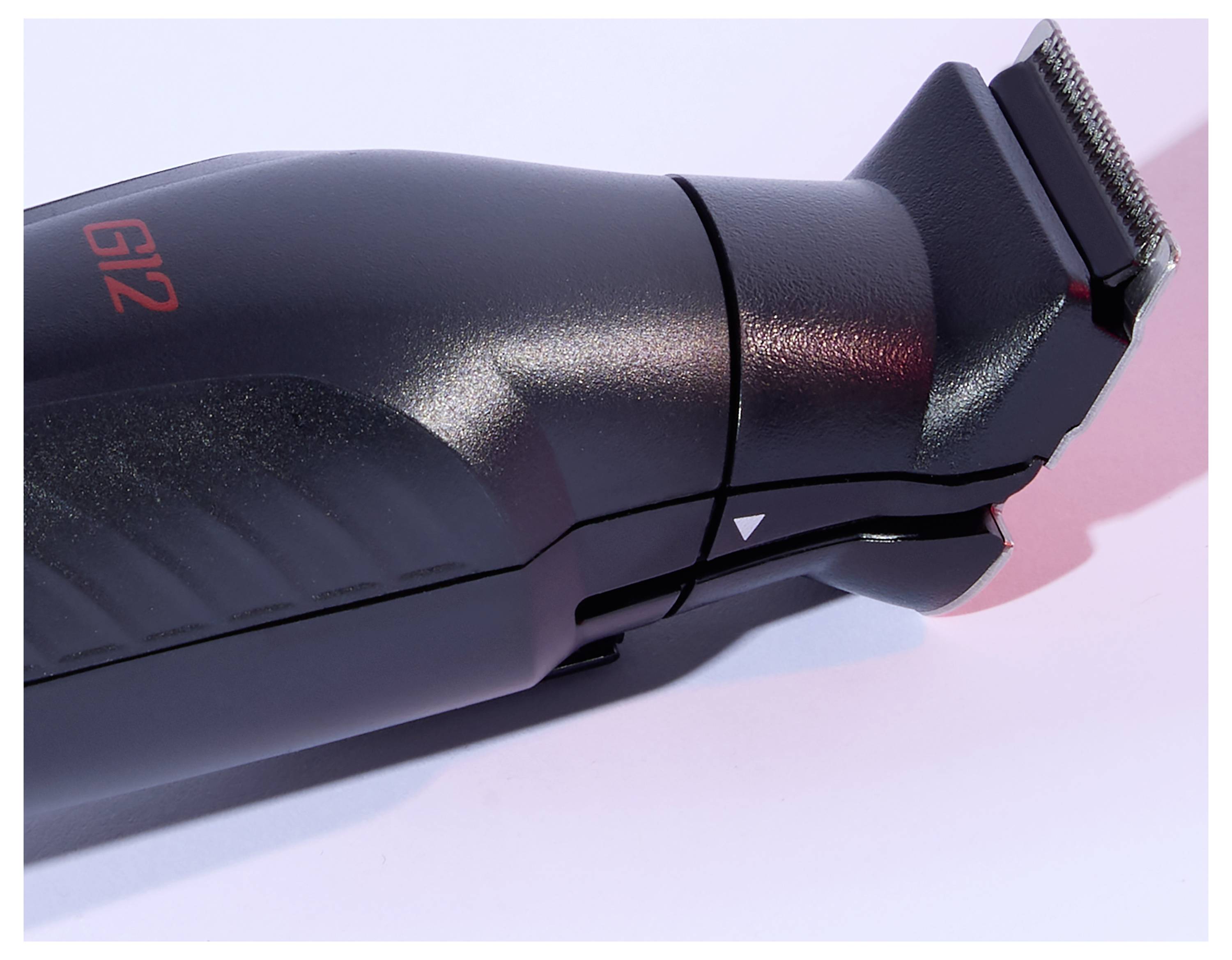 Eine Nahaufnahme einer schwarzen elektrischen Haarschneidemaschine mit sichtbaren Klingen, die vor einem weiß-rosa Hintergrund abgebildet ist.