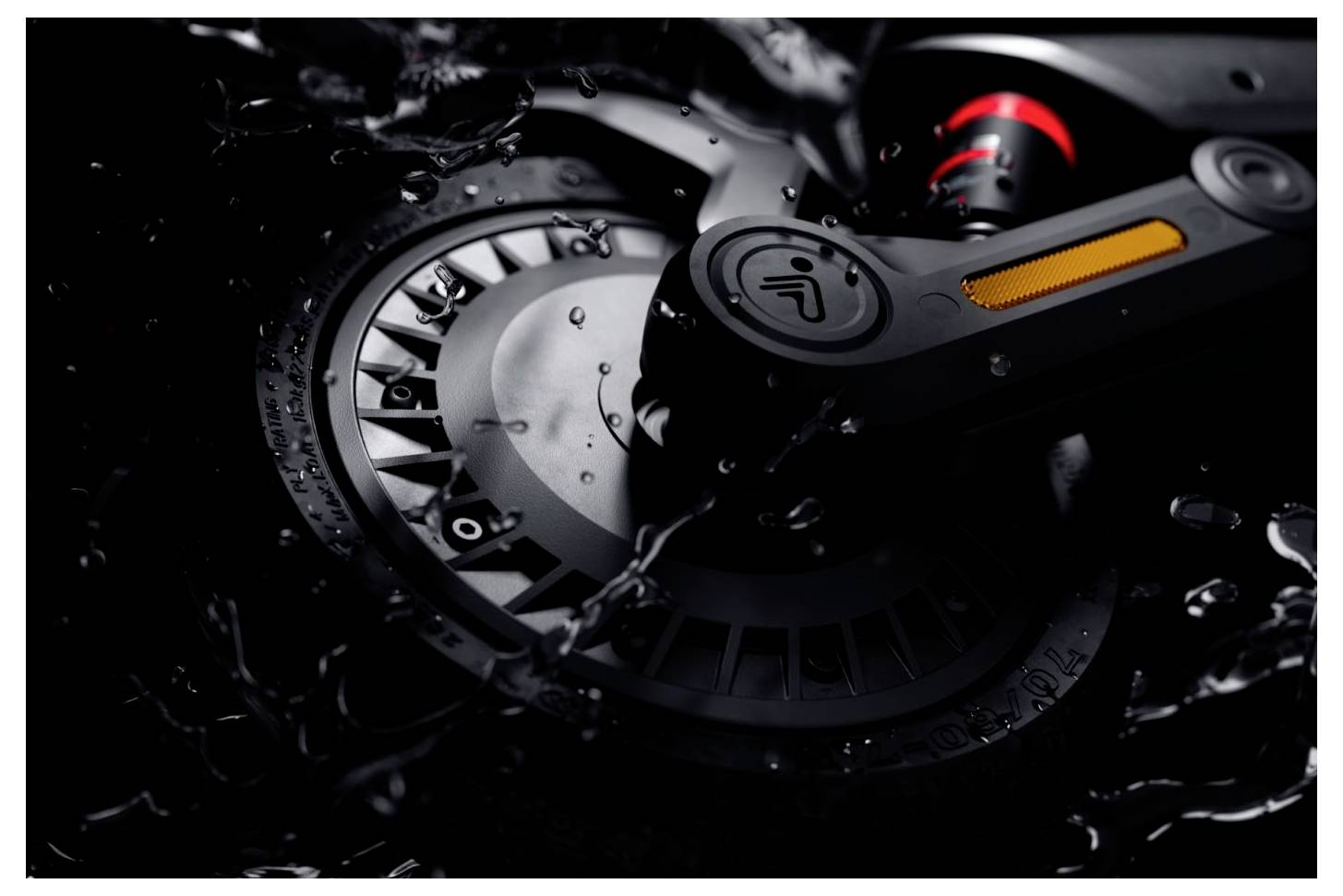 Eine Nahaufnahme eines schlanken schwarzen Elektroskateboard-Rads mit Wassertropfen, mit einem beleuchteten orangefarbenen Reflektor und einem roten Akzent.