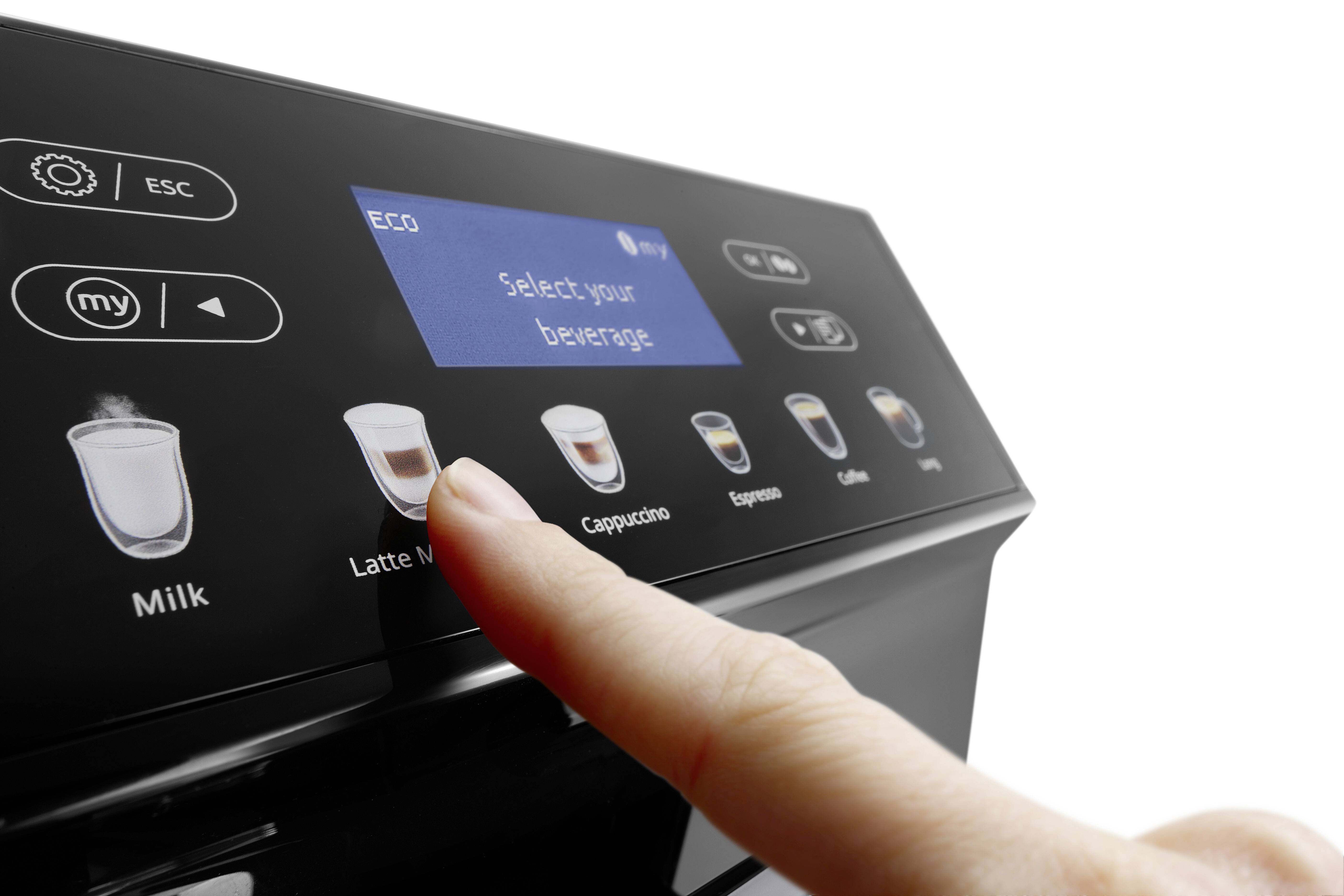Ein Finger drückt die Option 'Latte Macchiato' auf dem Touchpanel einer Kaffeemaschine, wobei verschiedene Kaffeearten auf dem Bildschirm angezeigt werden.