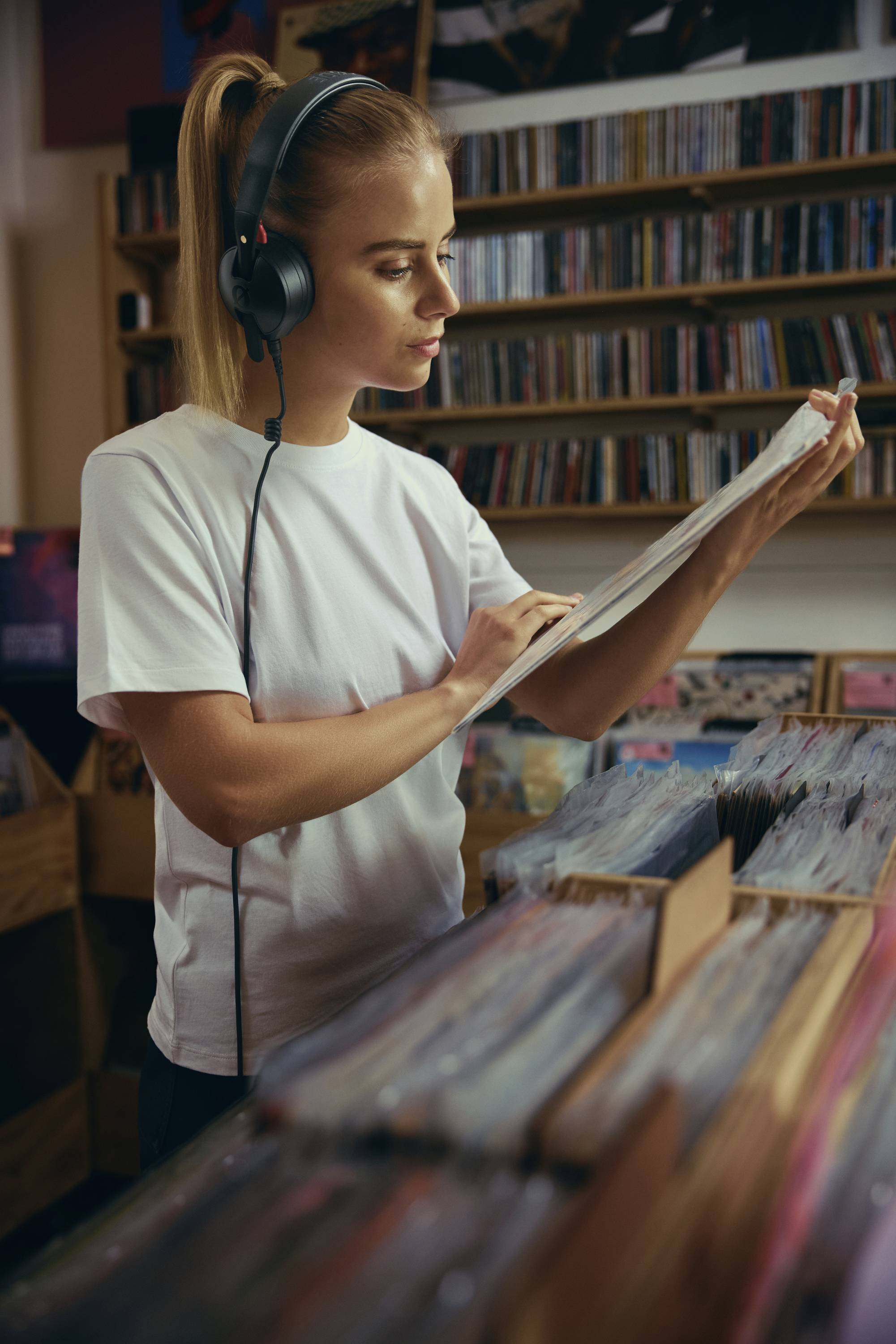 Eine Person mit Kopfhörern durchstöbert Schallplatten in einem Plattengeschäft, umgeben von Regalen voller Alben.