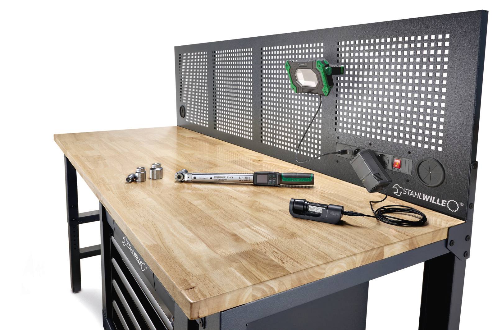 Werkbank mit Holzplatte und schwarzer Metallgelochttafel, auf der eine grüne Lampe steht. Werkzeuge auf der Oberfläche umfassen einen Drehmomentschlüssel und Steckschlüssel.