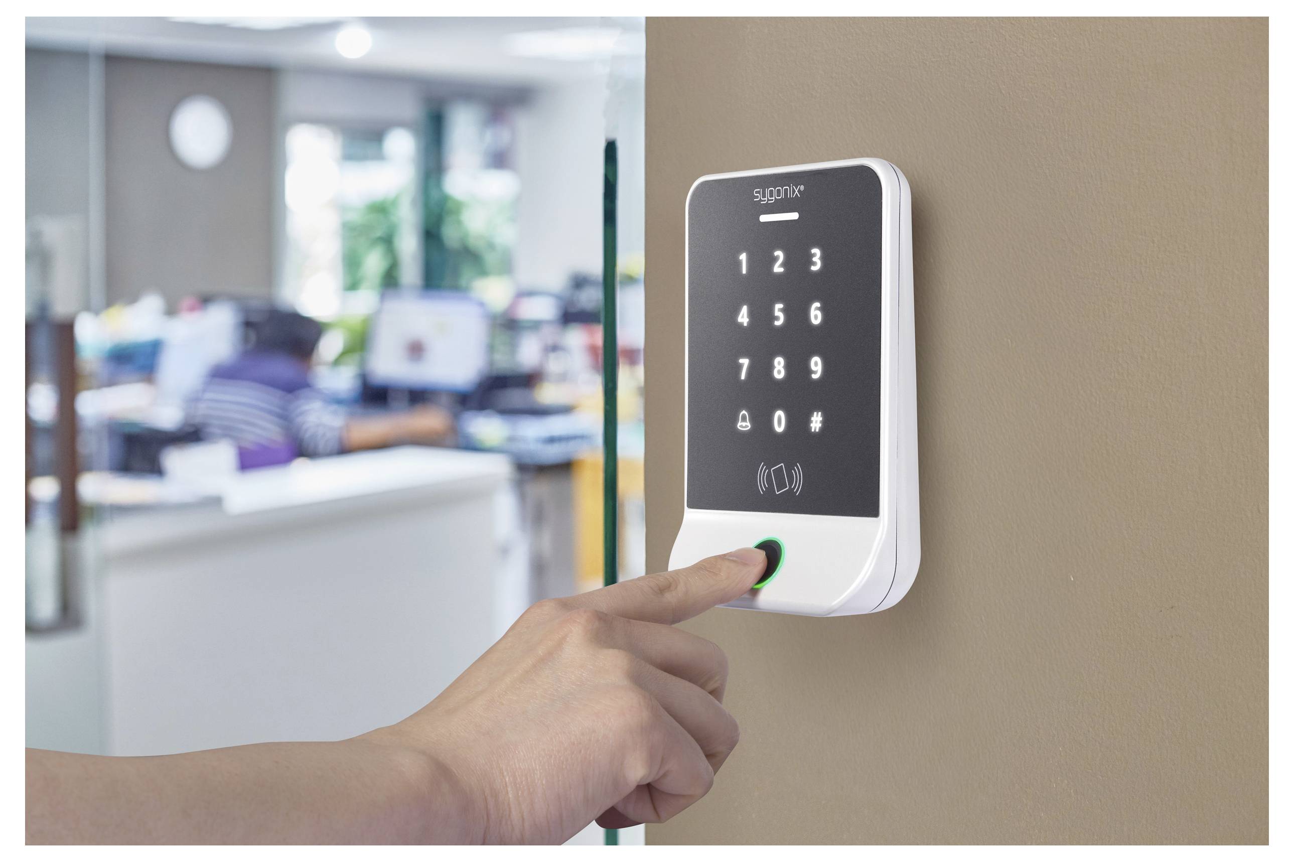 Die Hand einer Person drückt eine Taste auf einem an der Wand montierten Sicherheits-Tastenfeld mit Zahlen und Kartenlesefläche in einer Büroumgebung.