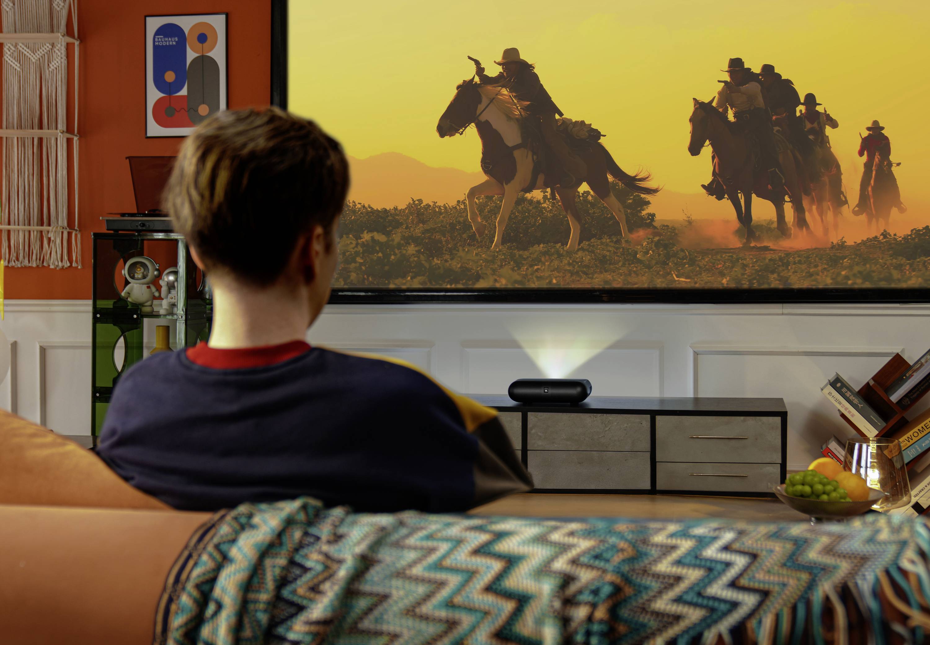 Eine Person schaut in einem gemütlichen, dekorierten Wohnzimmer einen Western-Film mit Reitern zu Pferd auf einem großen Bildschirm.