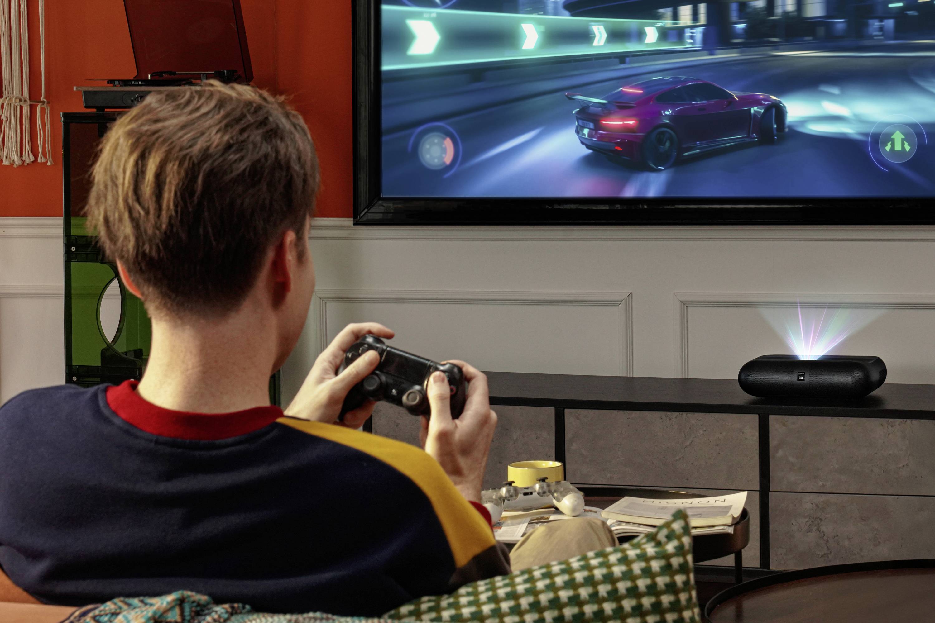 Eine Person spielt ein Rennvideospiel auf einem großen Bildschirm und bedient dabei einen Gamecontroller. Ein Auto rast auf einer leuchtenden, farbenprächtig beleuchteten Strecke.