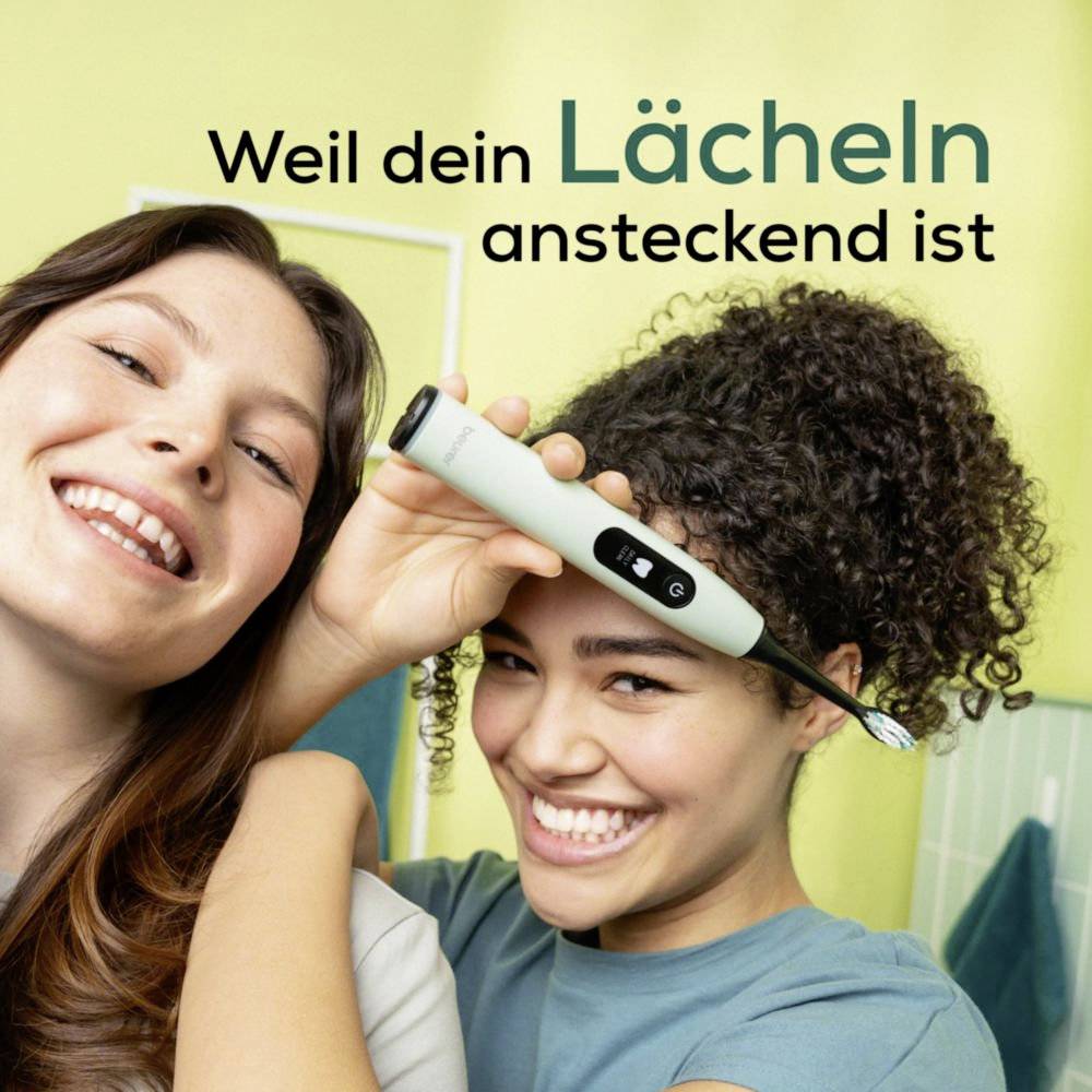 Zwei Frauen lächeln in die Kamera, während eine eine elektrische Zahnbürste hält. Deutscher Text lautet: 'Weil dein Lächeln ansteckend ist.'