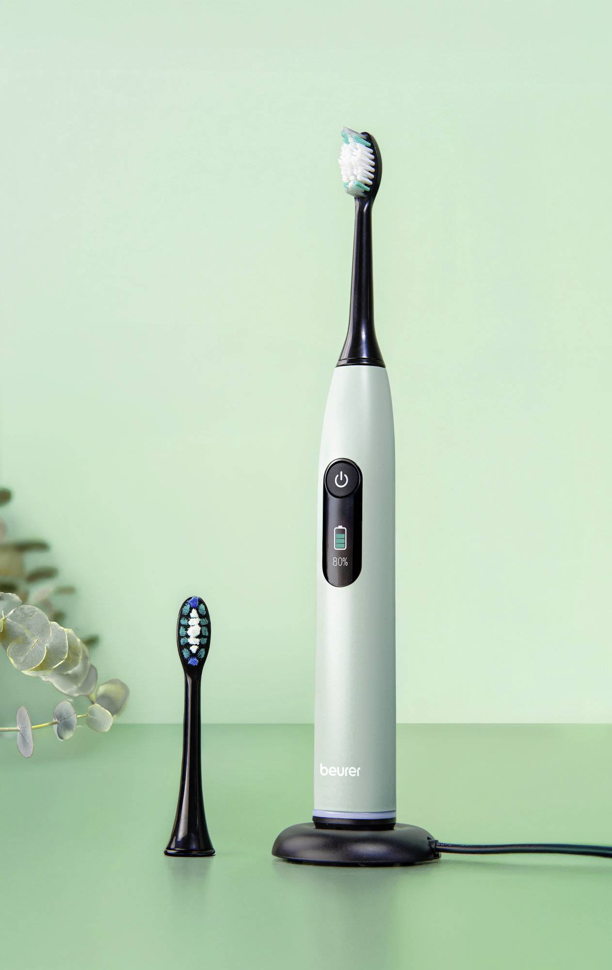 Elektrische Zahnbürste mit zusätzlichem Bürstenkopf auf einer Ladestation vor einem hellgrünen Hintergrund.