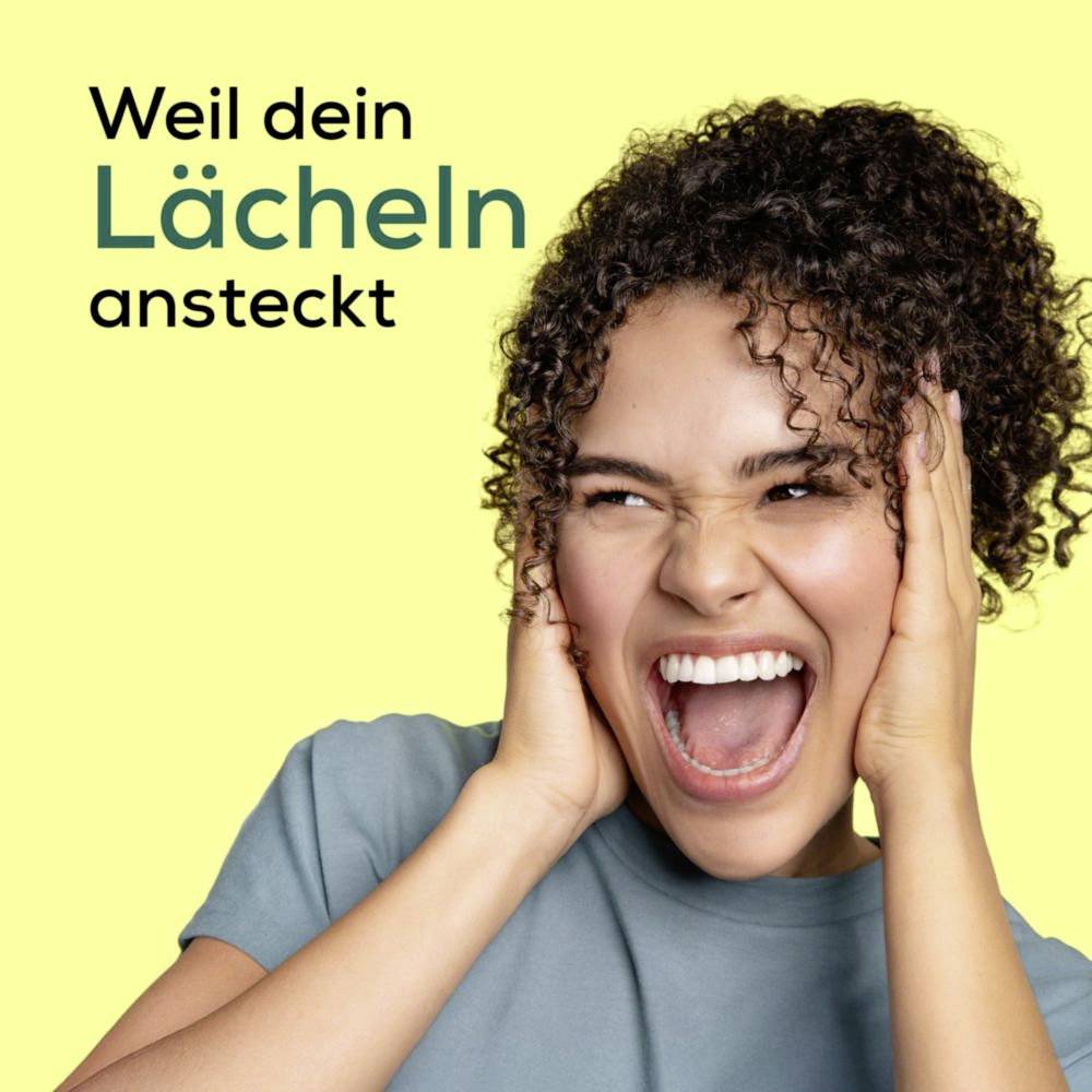 Eine Frau mit lockigem Haar lächelt breit und hält sich vor Aufregung das Gesicht. Der Text lautet 
