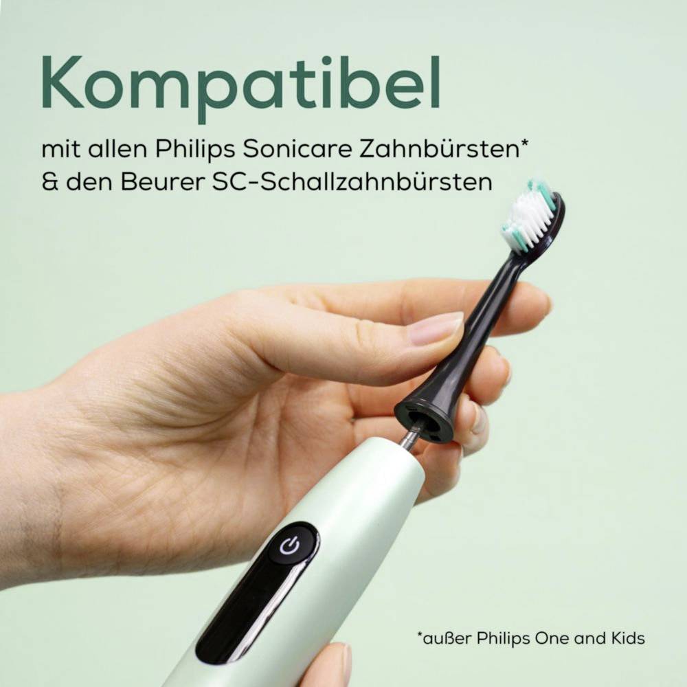 Eine Hand hält eine graue elektrische Zahnbürste mit schwarzen Borsten vor einem grünen Hintergrund. Der Text lautet: 'Kompatibel mit allen Philips Sonicare Zahnbürsten* & den Beurer SC-Schallzahnbürsten'.