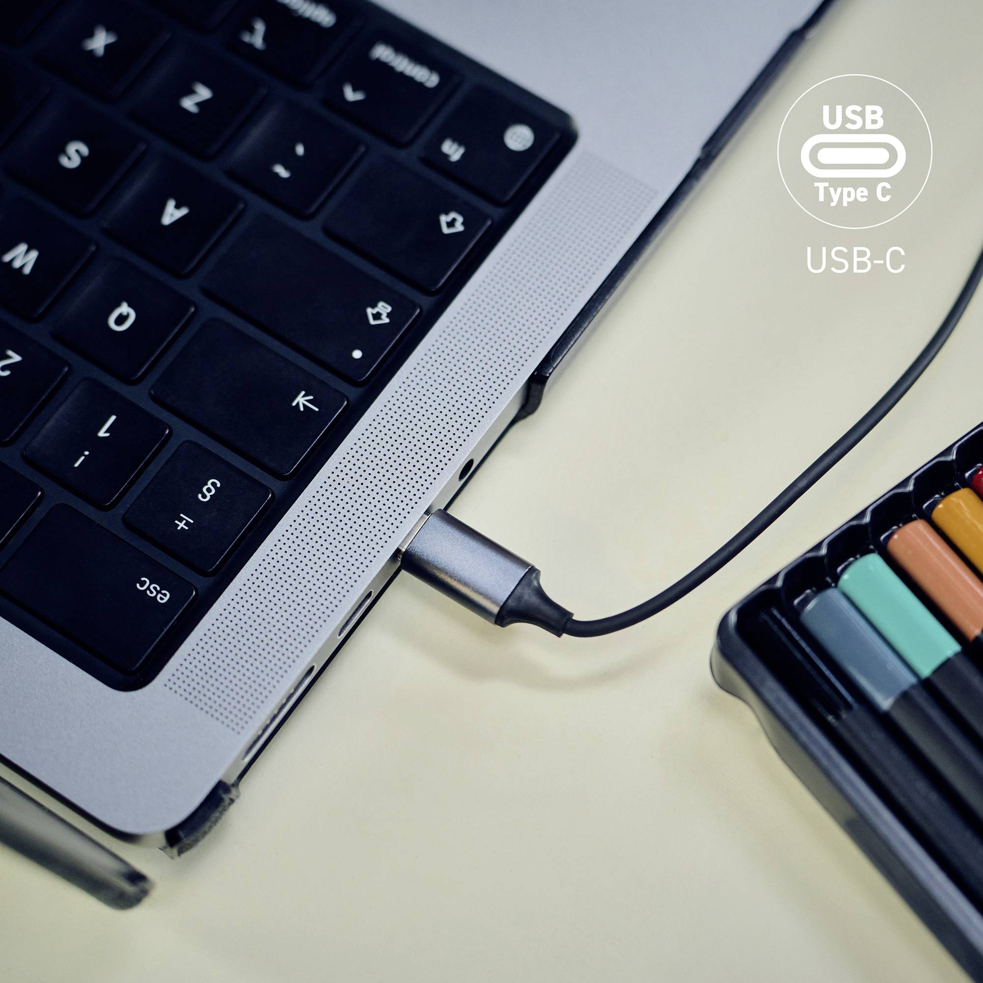 Ein USB Typ-C-Kabel ist an einen Laptop angeschlossen, umgeben von bunten Markern auf einem Schreibtisch, was die Vielseitigkeit von USB-C-Anschlüssen unterstreicht.