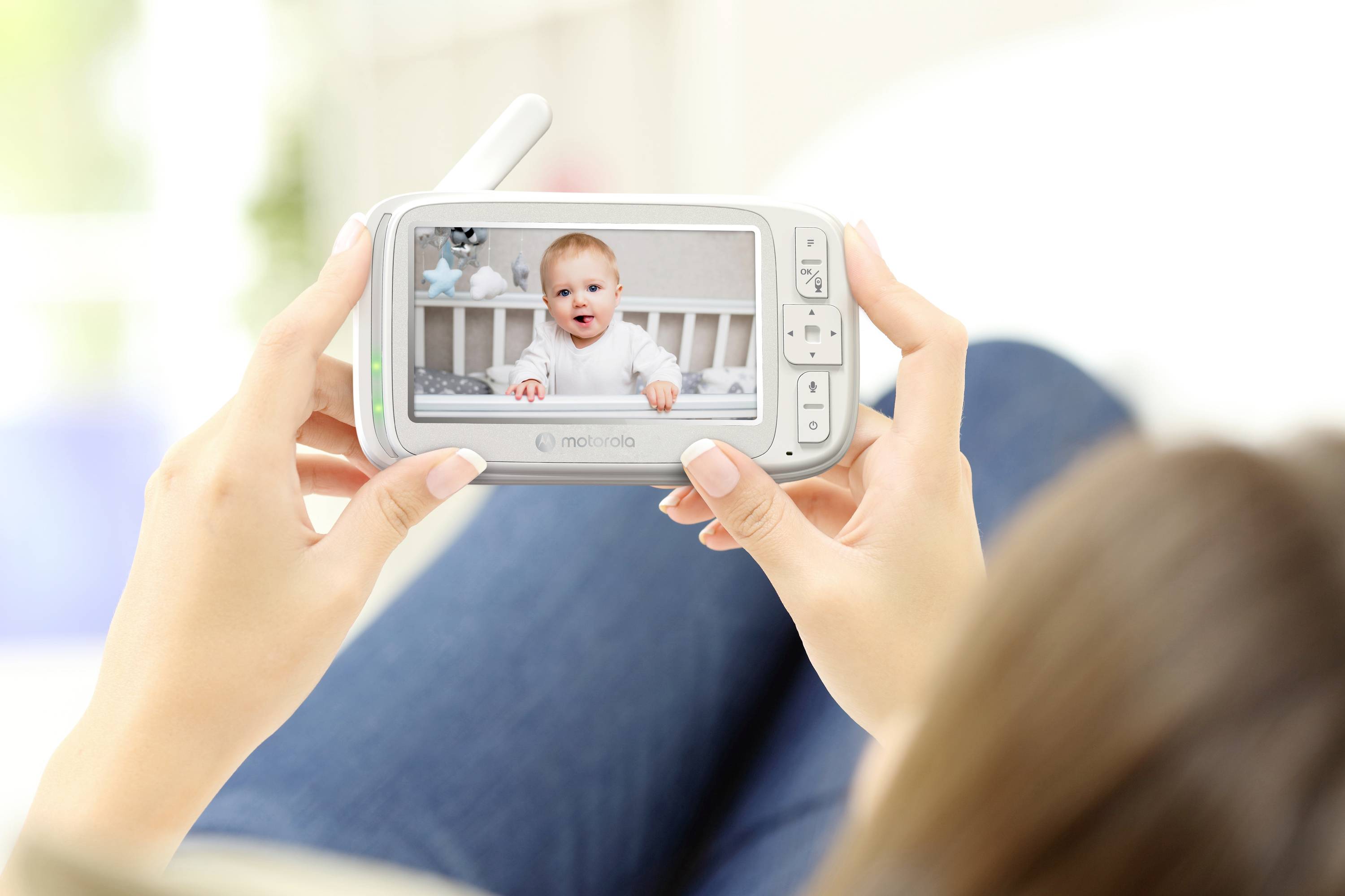 Eine Person hält einen Babyphone, auf dem ein lachendes Baby in einem Kinderbett zu sehen ist und so die Fernüberwachung von Babys darstellt.