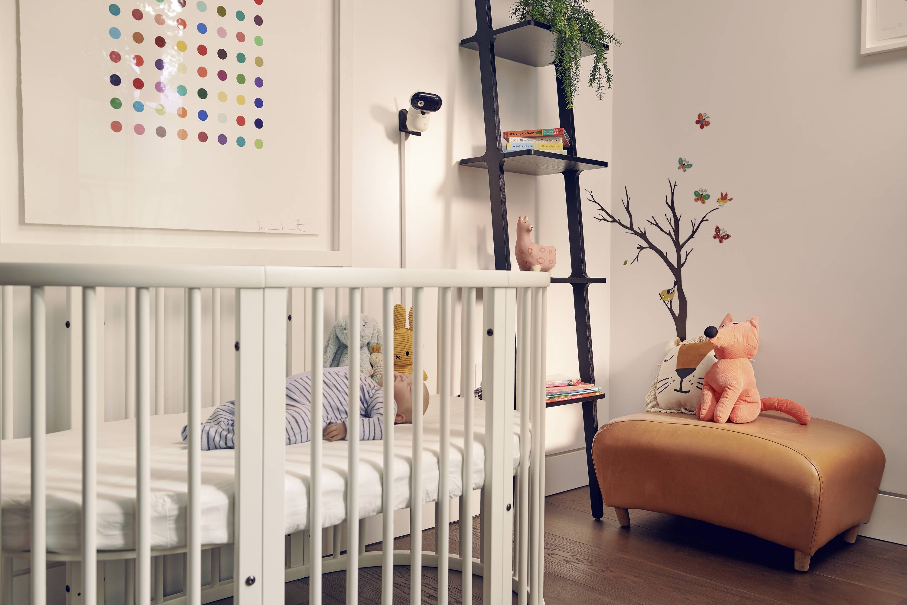 Ein Babyzimmer mit einem weißen Gitterbett, verspielten Kuscheltieren, einem an der Wand montierten Kunstwerk und einem gemütlichen Sessel, der eine behagliche, farbenfrohe Atmosphäre schafft.