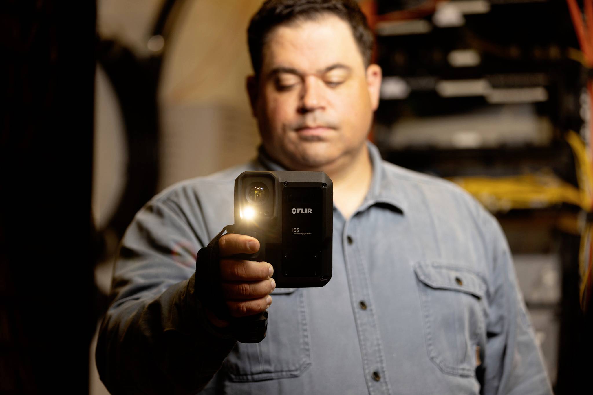 Eine Person, die eine Wärmebildkamera in einem industriellen Umfeld verwendet und sich darauf konzentriert, Temperaturmessungen von Ausrüstung im Hintergrund aufzunehmen.