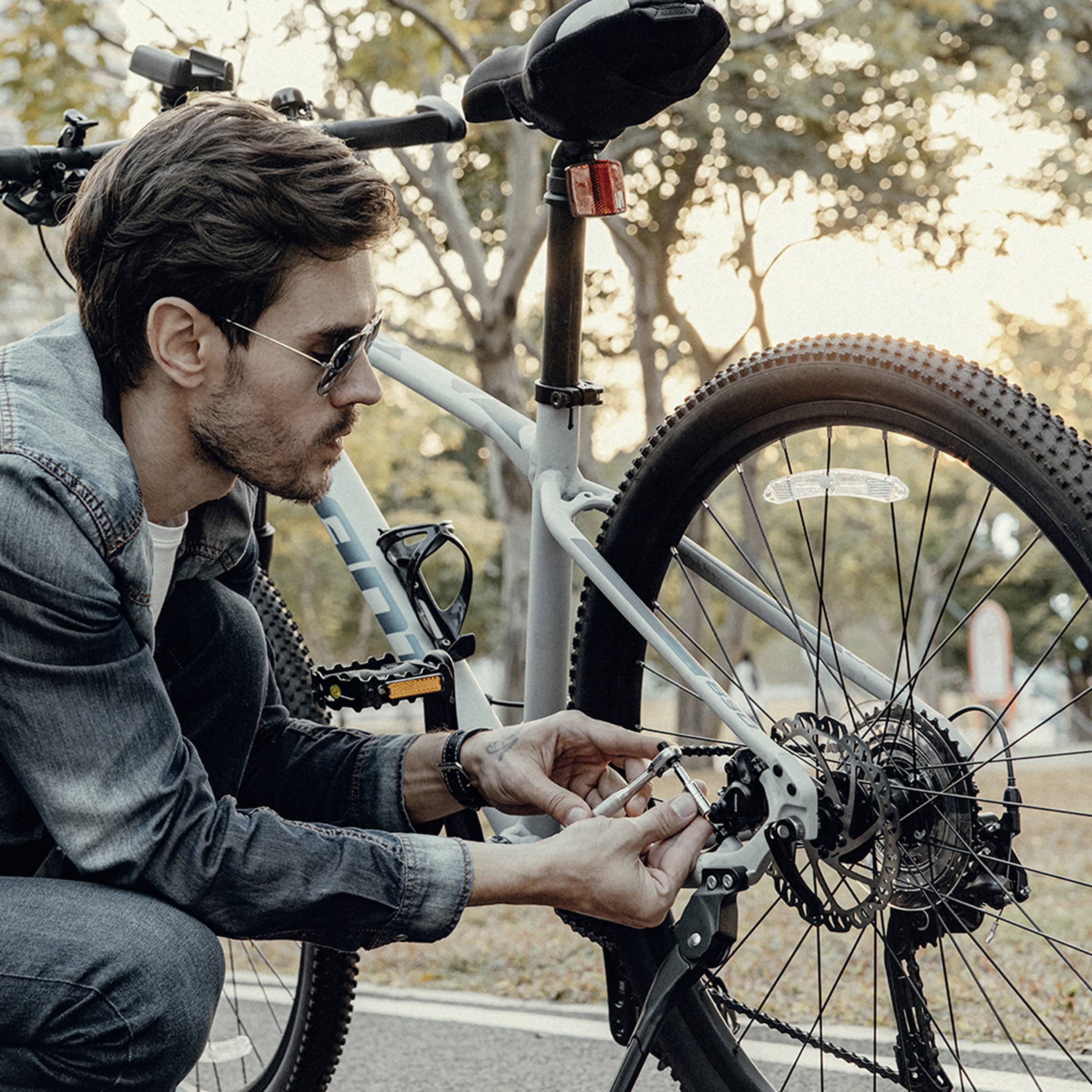 Eine Person in einer Jeansjacke justiert die Gänge eines Fahrrads, das in einer malerischen Parklandschaft geparkt ist, umgeben von Bäumen mit Herbstlaub.