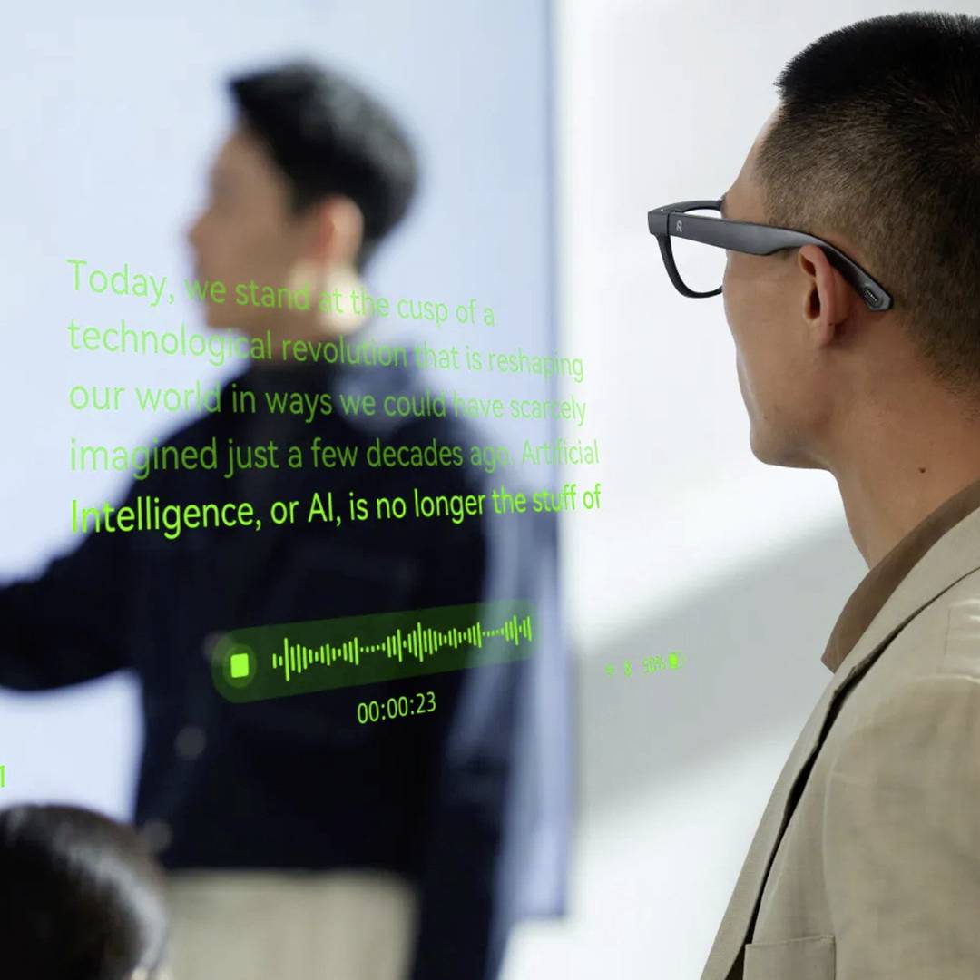 Ein Mann steht in der Nähe eines transparenten Bildschirms, auf dem Text über Technologie und KI angezeigt wird, während im Hintergrund eine weitere Person auf eine Tafel zeigt.