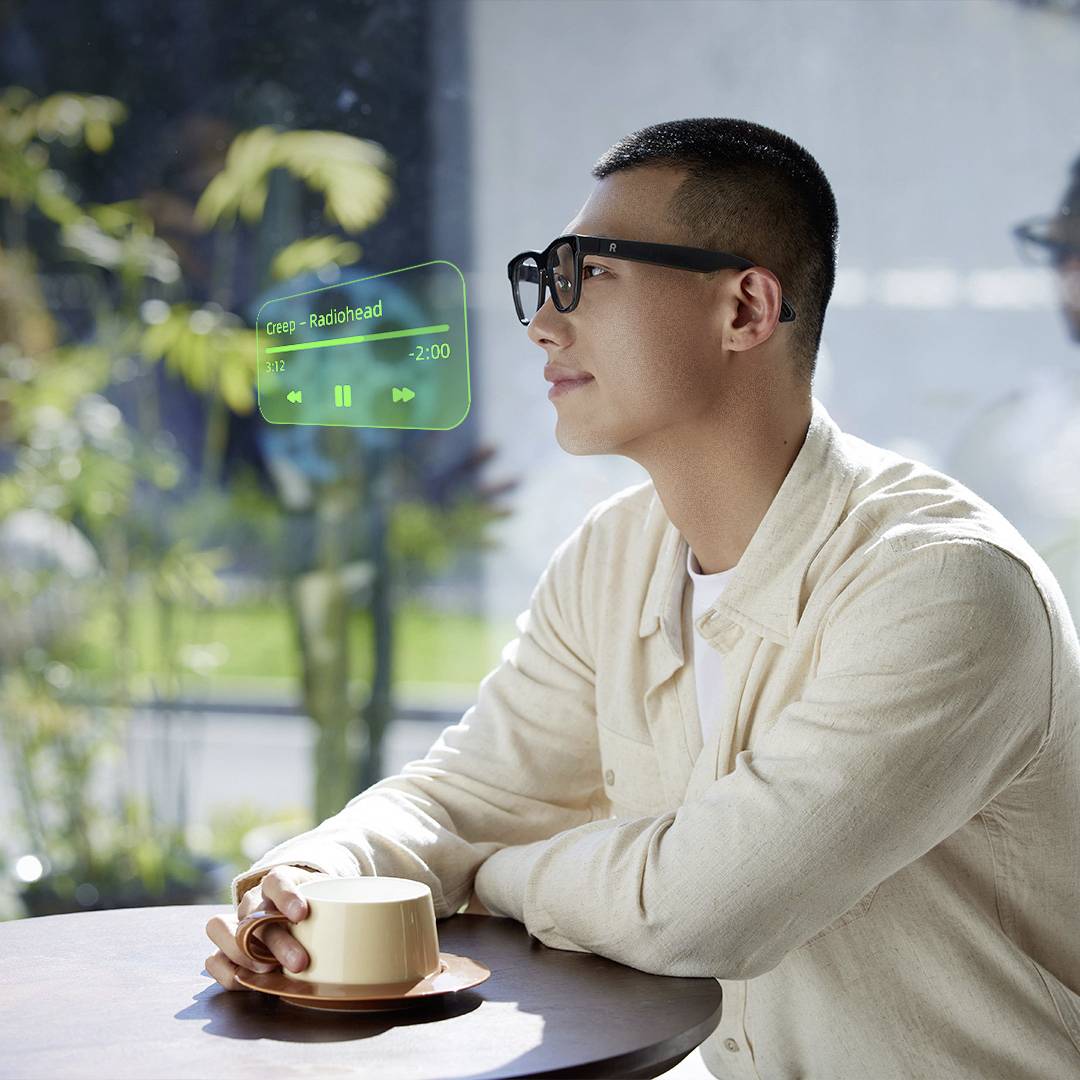 Ein Mann in einer weißen Jacke sitzt an einem Tisch und nutzt Augmented Reality, um eine Musikplayer-Schnittstelle anzuzeigen, auf der 