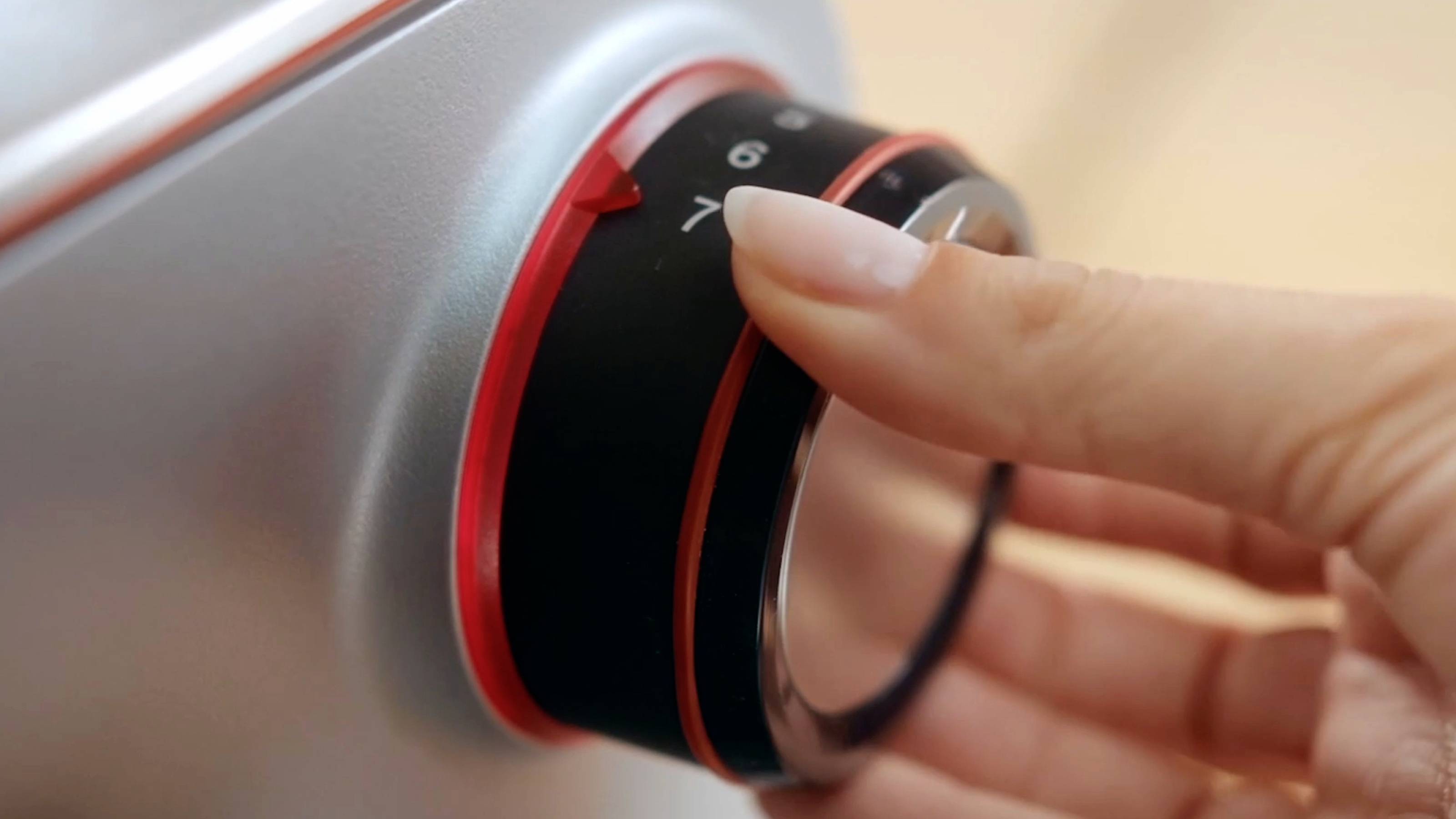 Eine Hand, die einen kreisrunden Drehknopf an einem metallenen Gerät dreht und mit Präzision und Kontrolle Einstellungen justiert.