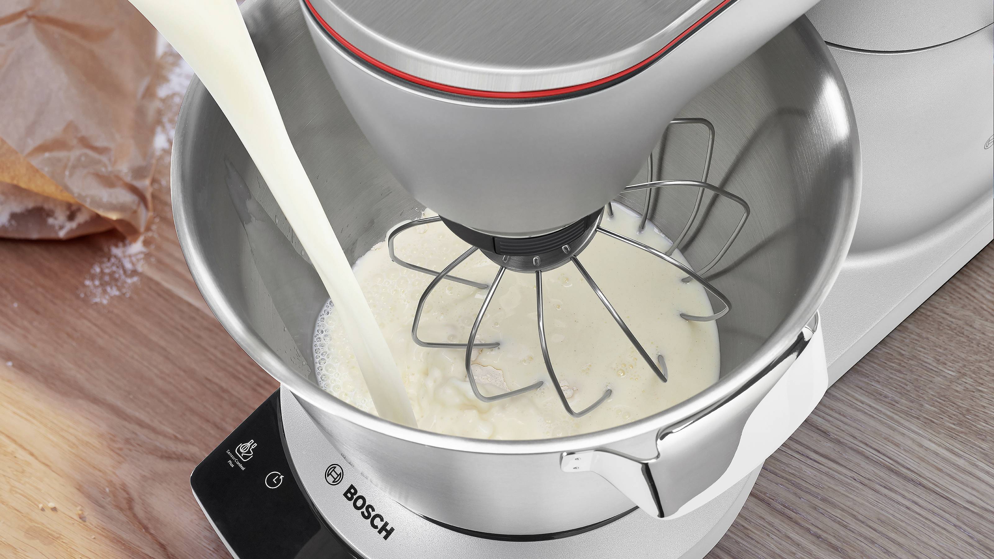 Ein Bosch-Standmixer, der Milch in eine Rührschüssel mit Schneebesen einfüllt.