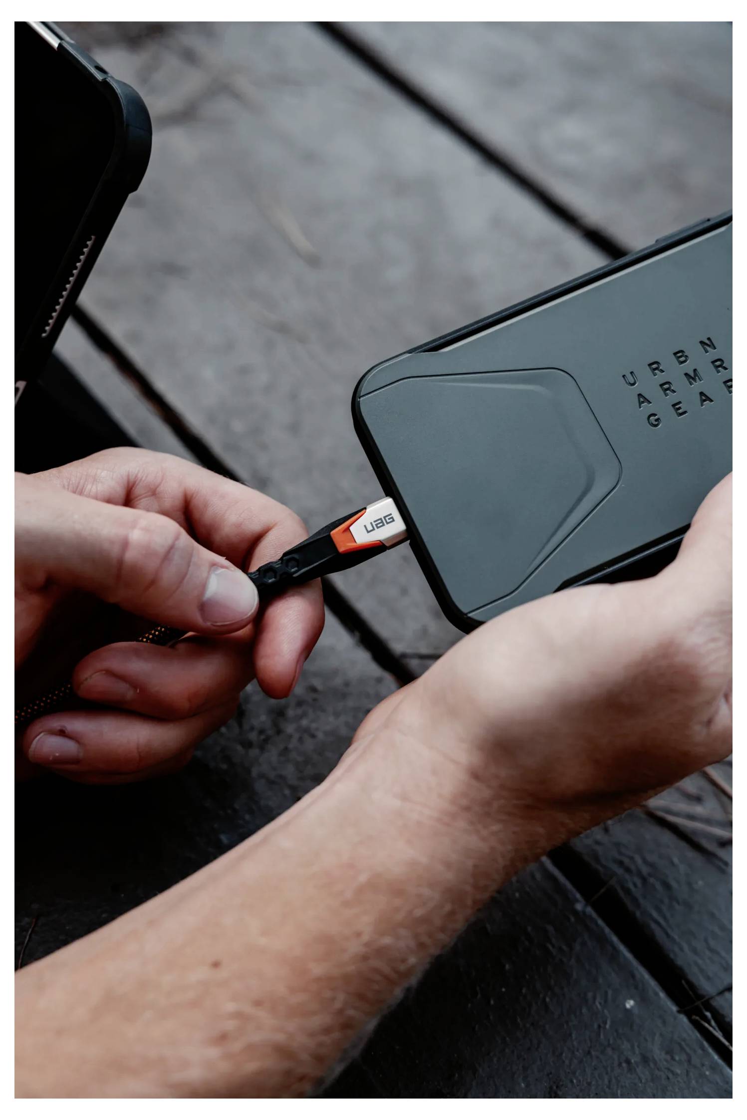 Eine Person steckt ein USB-Ladekabel in ein Smartphone auf einer Holzoberfläche.