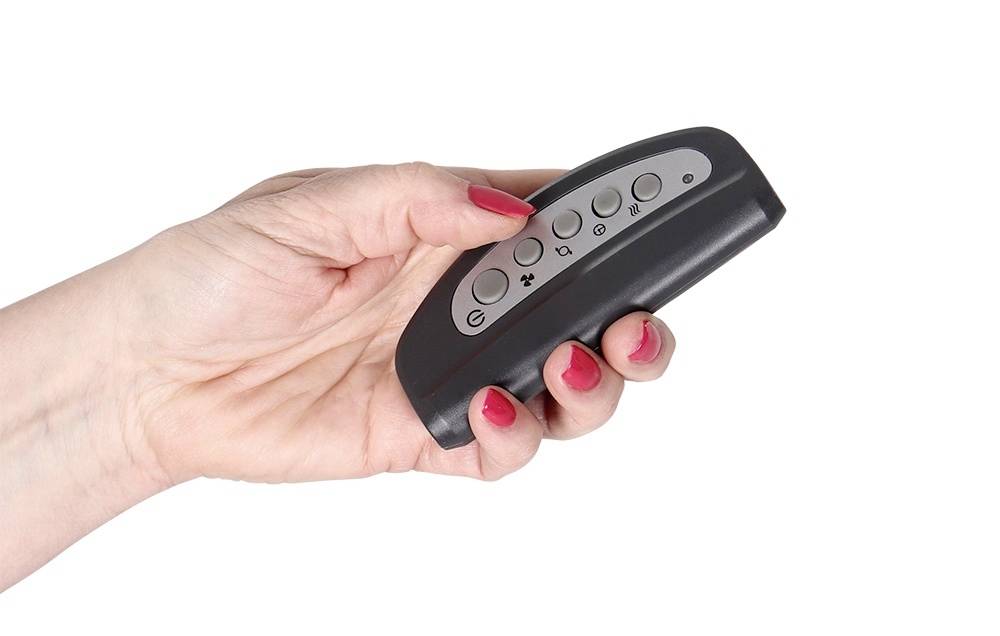 Eine Hand mit roten Nägeln hält eine schwarze Fernbedienung mit mehreren Knöpfen vor einem weißen Hintergrund.